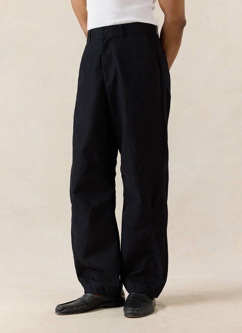 A model wears the Percival Milo Relaxed Barrel Leg Trousers in black, styled with a white ribbed top and black loafers.
