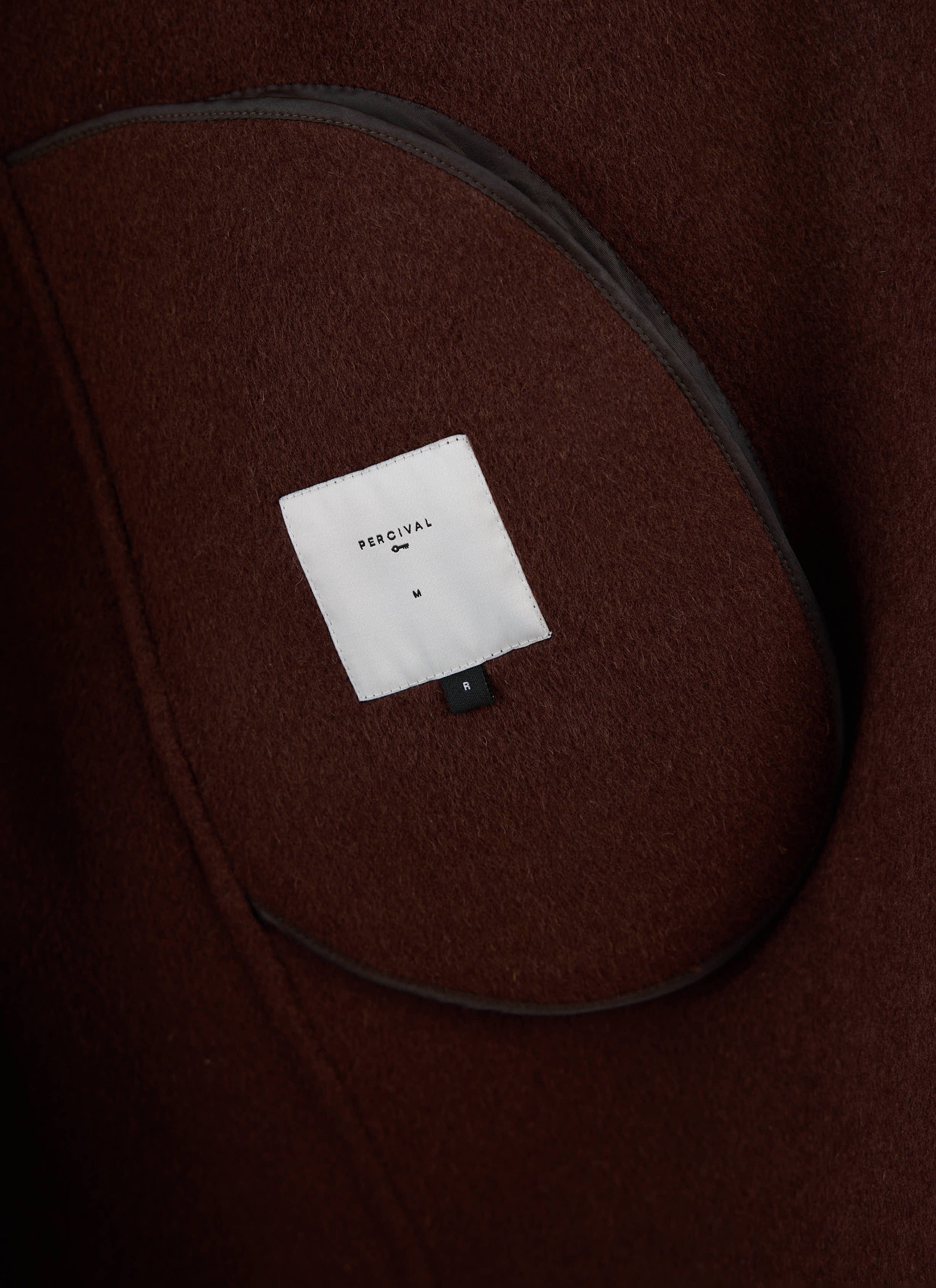 A close-up of the interior brand label inside the brown fleck Minnesota Overcoat from Percival.