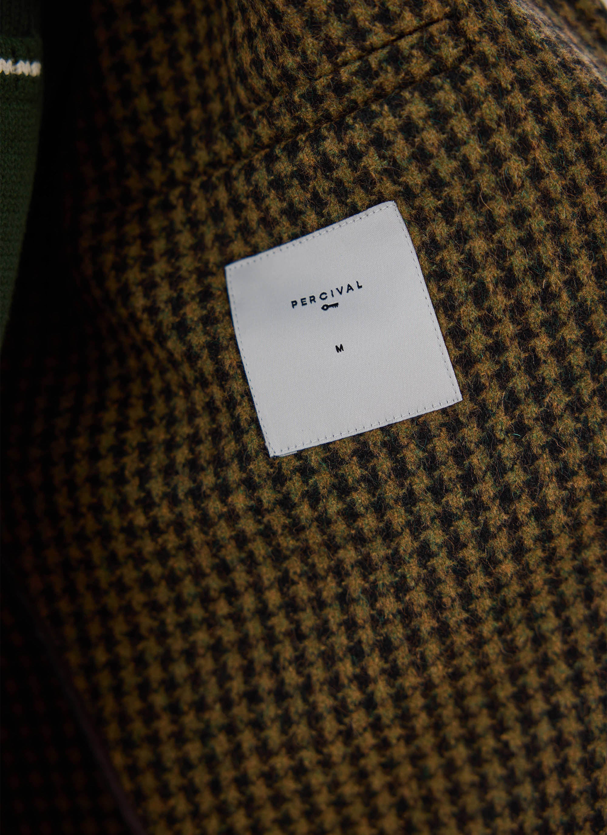 A close-up of the interior brand label inside the Watcher Check Minnesota Overcoat from Percival.