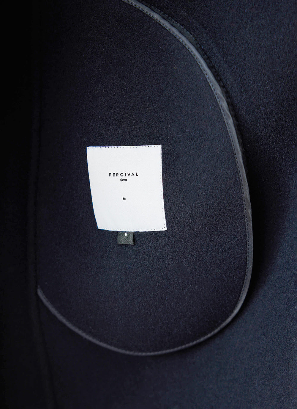 A close-up of the interior label and navy wool fabric of the Percival Minnesota Overcoat.