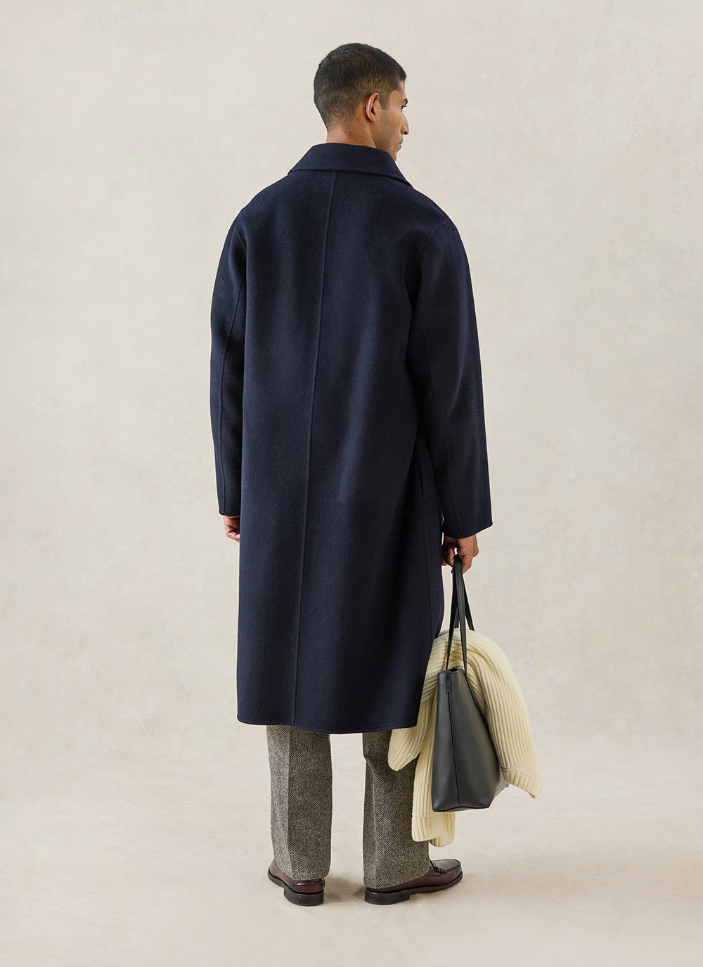 A rear-view shot of a model wearing the navy wool Minnesota Overcoat from Percival, holding a black tote bag.