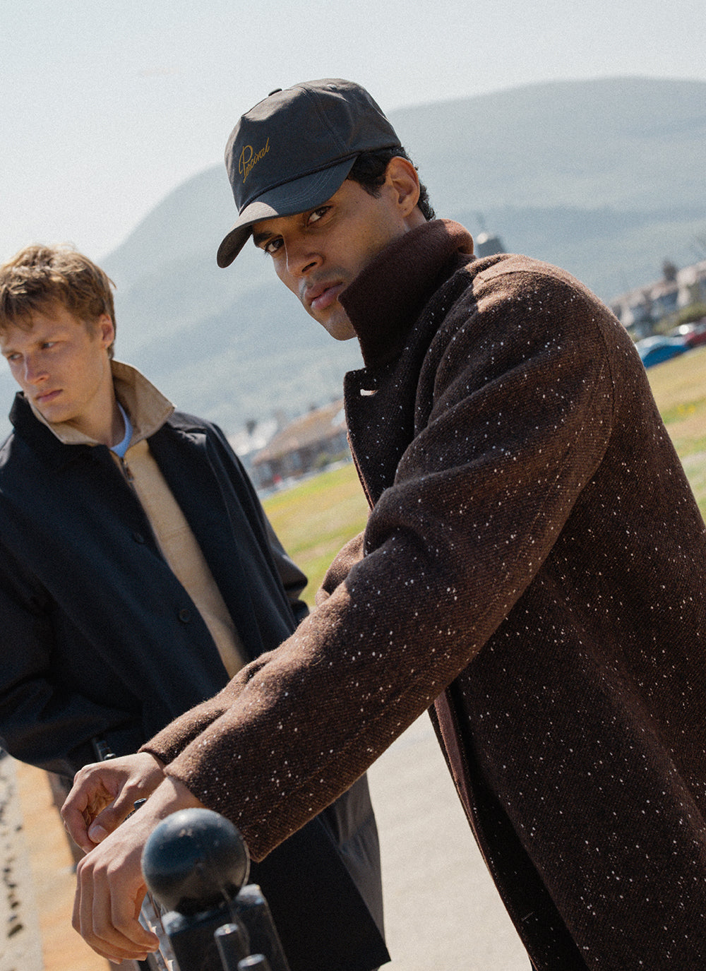 A model wearing the charcoal Percival Luther soft trucker cap and brown fleck Minnesota overcoat outdoors.