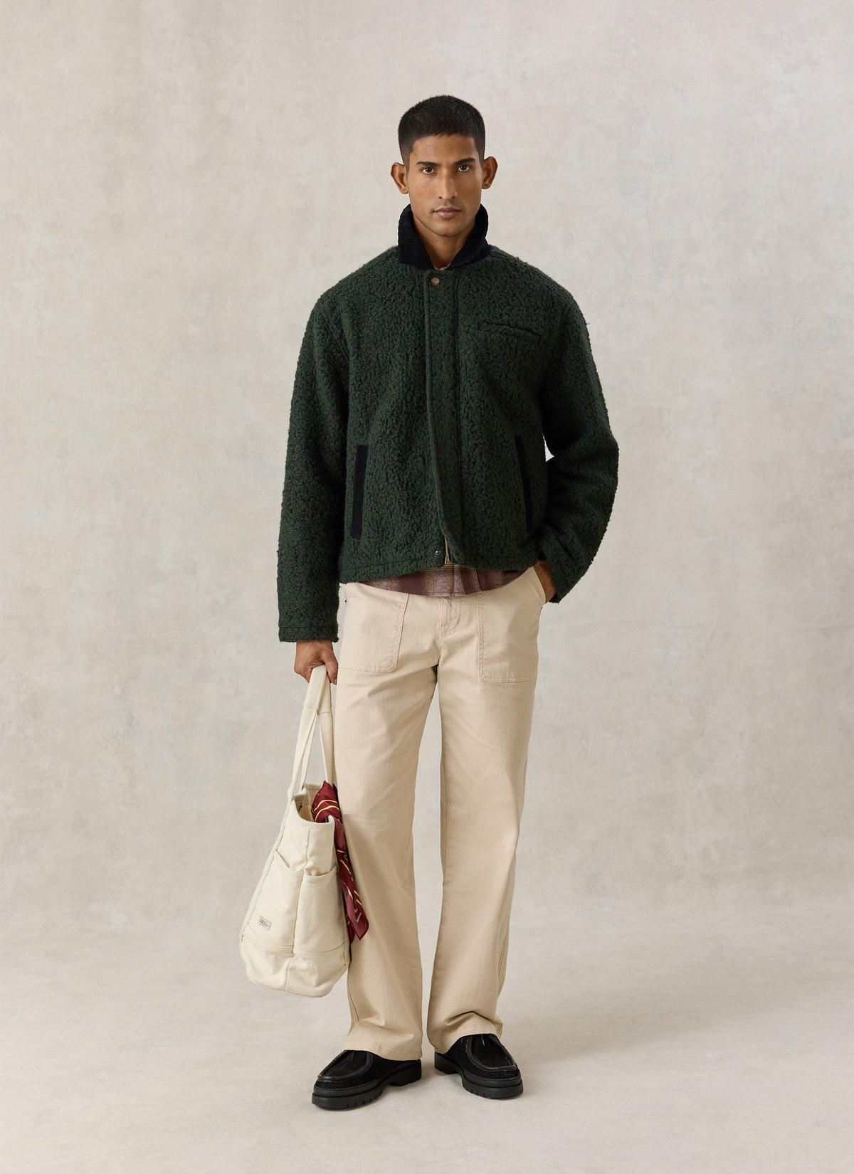 A model wearing the Percival forest green Murrey fleece jacket with a cord collar, cream trousers, and holding a tote bag.