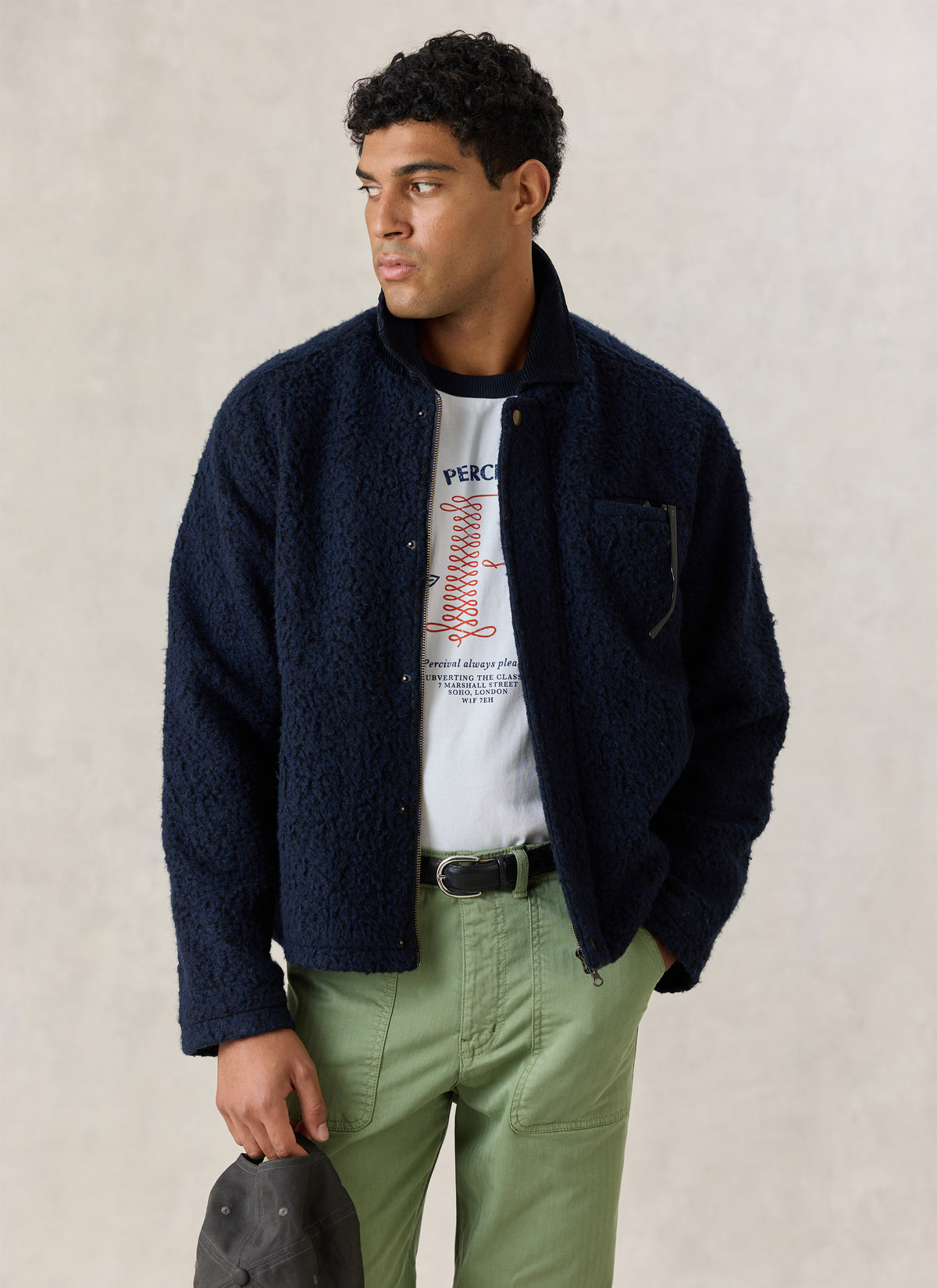 Model wearing the navy Percival Murrey fleece jacket with a cord collar, white t-shirt, and green trousers.