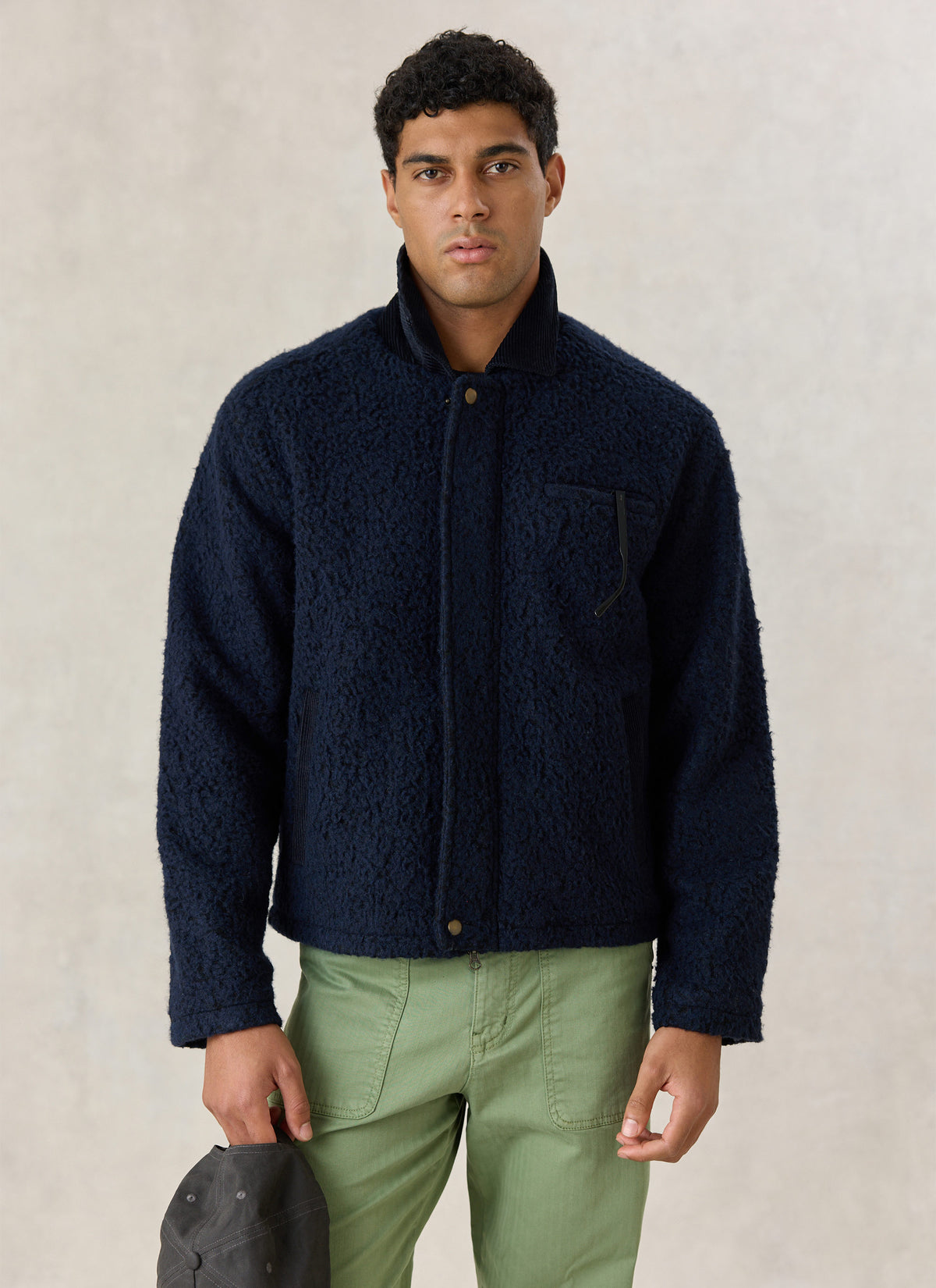 A model wearing the Percival navy wool-blend fleece jacket with a contrast cord collar and green trousers.