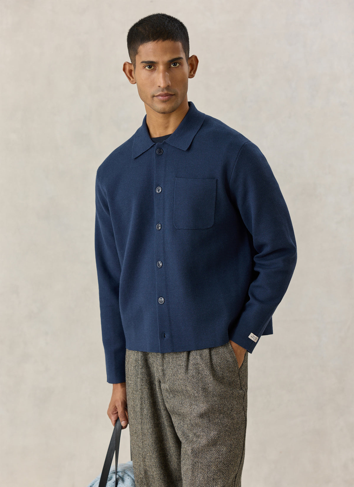 A model wearing the navy Percival Nixon knit collared cardigan with a button front, paired with patterned trousers.