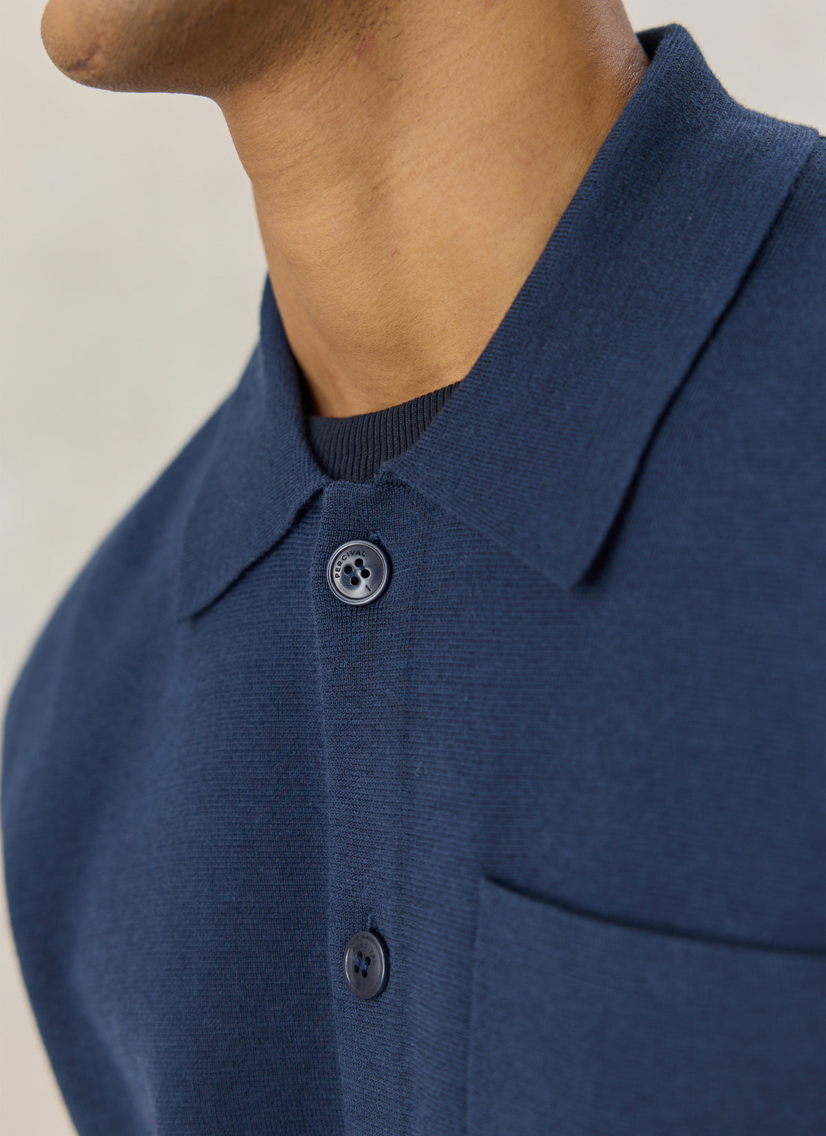A close-up of the Percival Nixon navy blue knit collared cardigan, highlighting the button front and chest pocket.