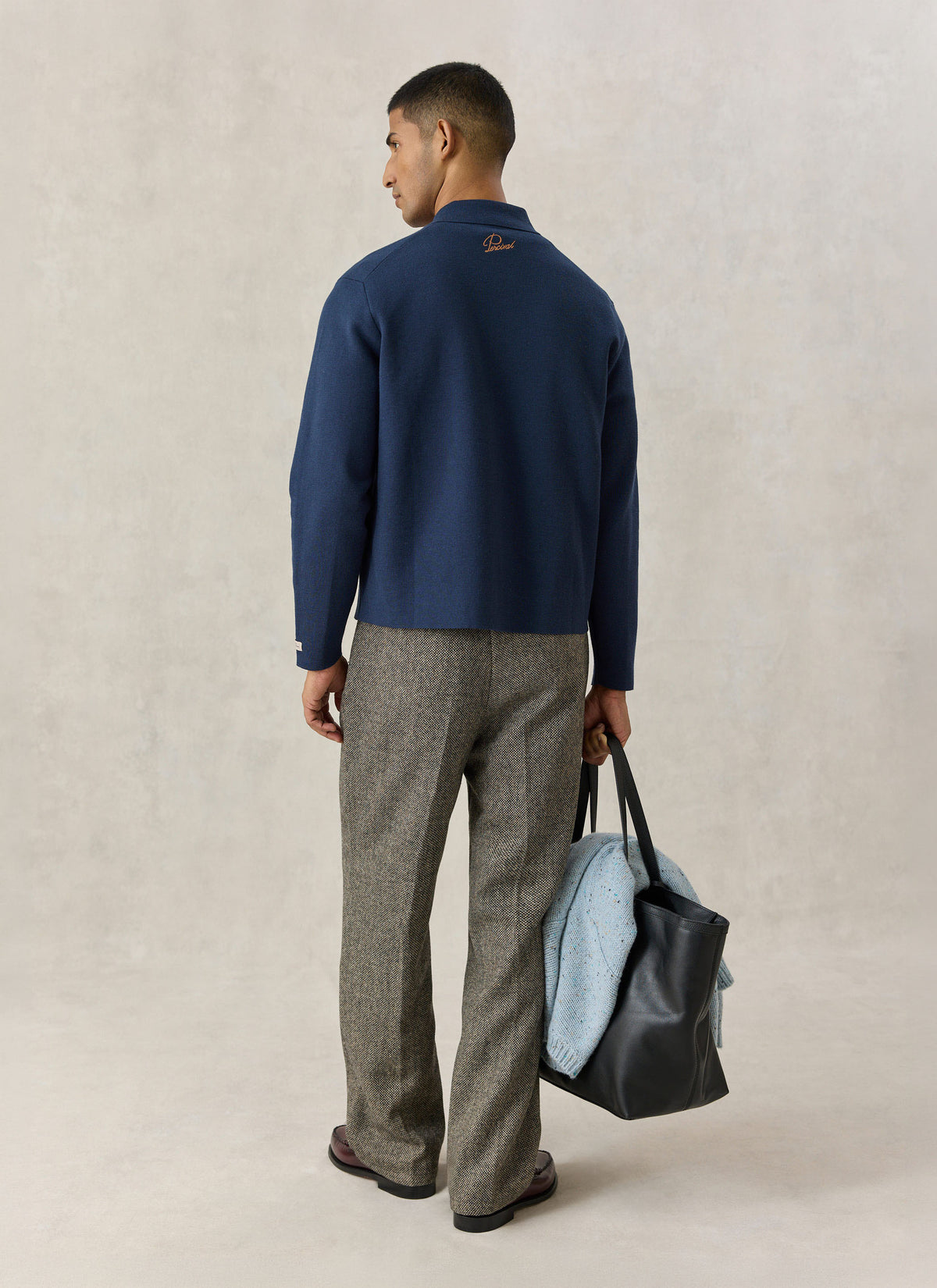 Model wearing the Percival navy blue Nixon cardigan from the back, showing neck embroidery and patterned trousers.
