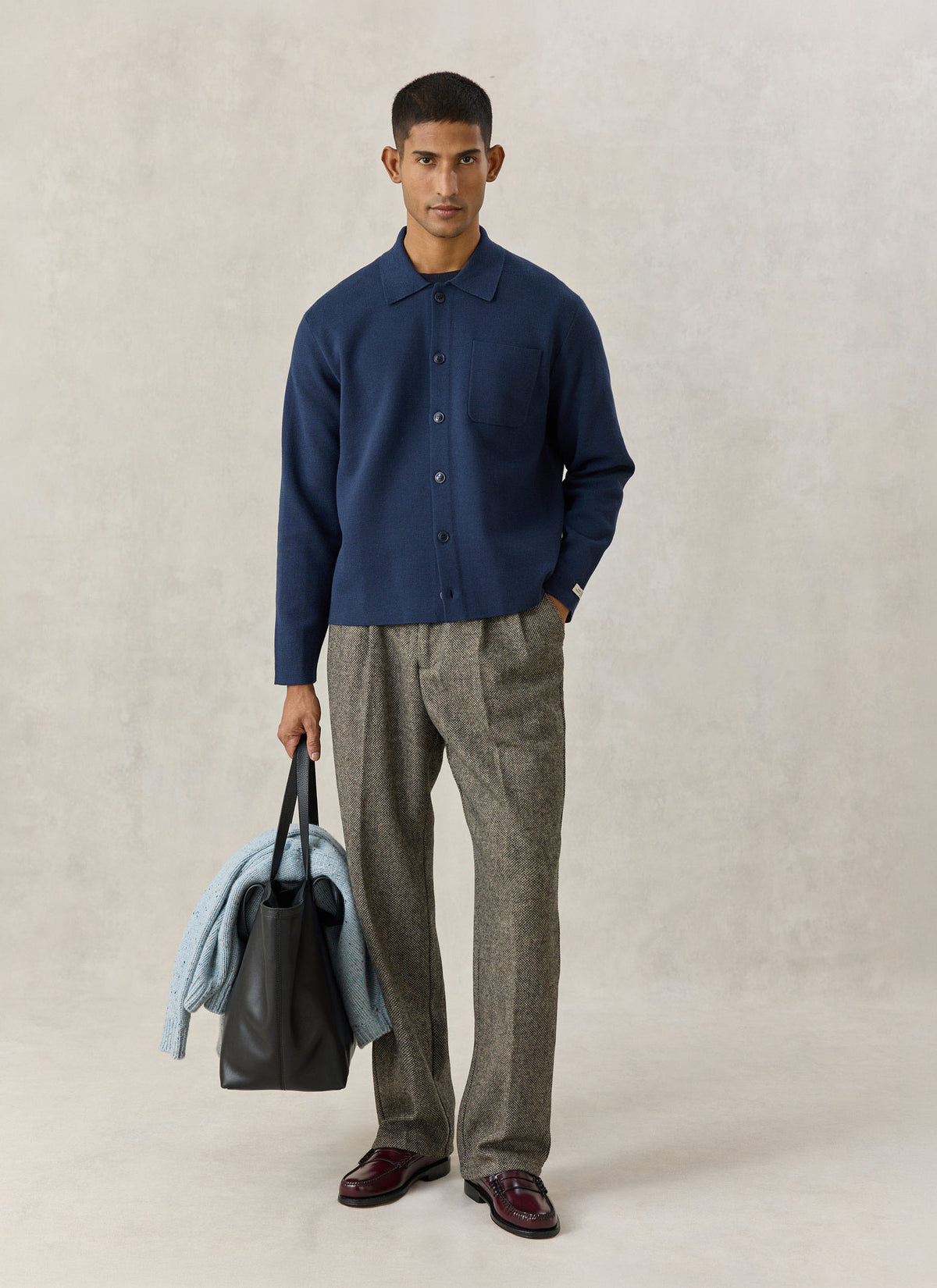 A model wearing the navy blue Percival Nixon knit collared cardigan with patterned trousers, holding a black leather bag.