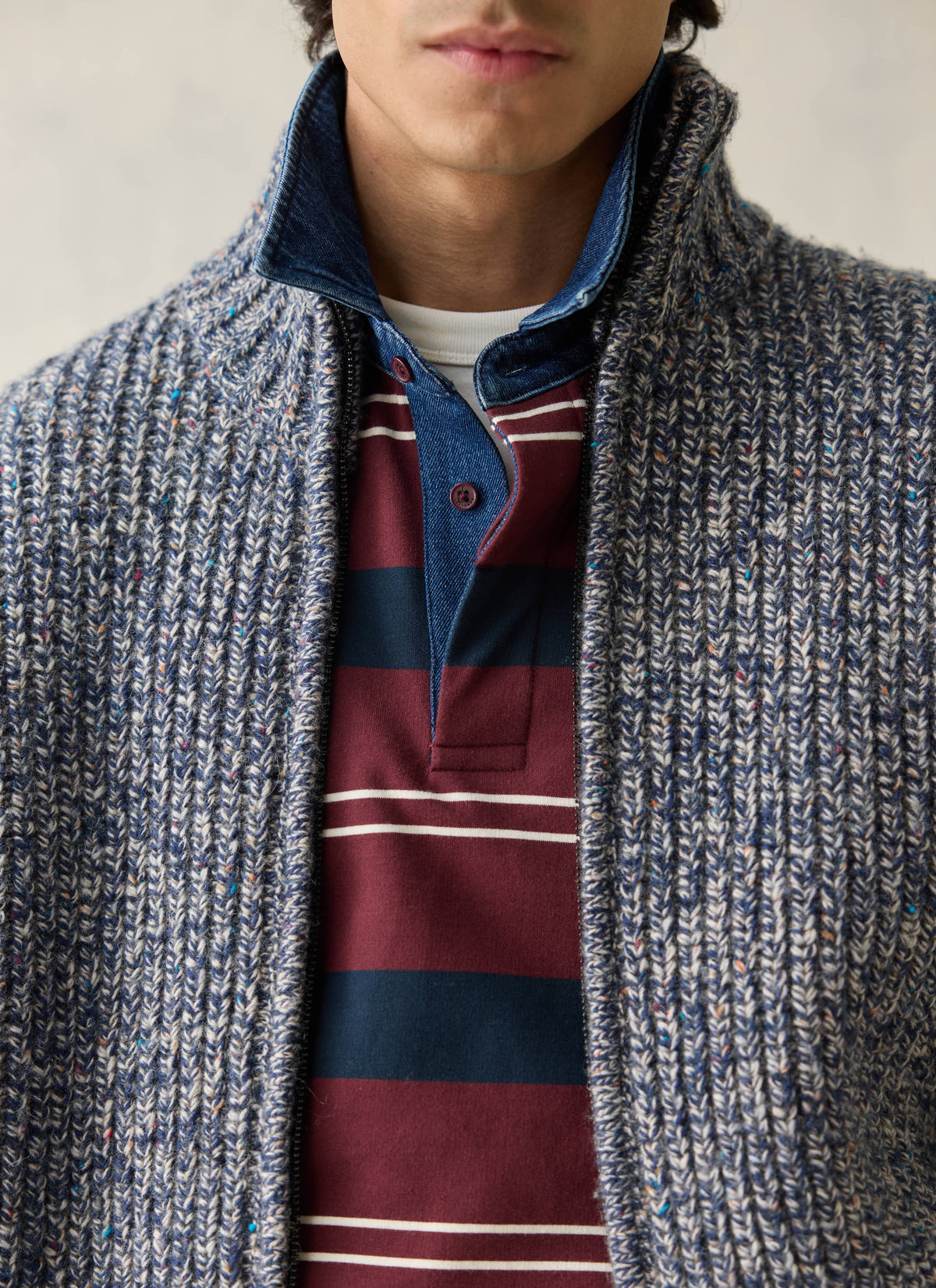A close-up of the Percival Norton blue fleck fisherman cardigan layered over a striped polo shirt.