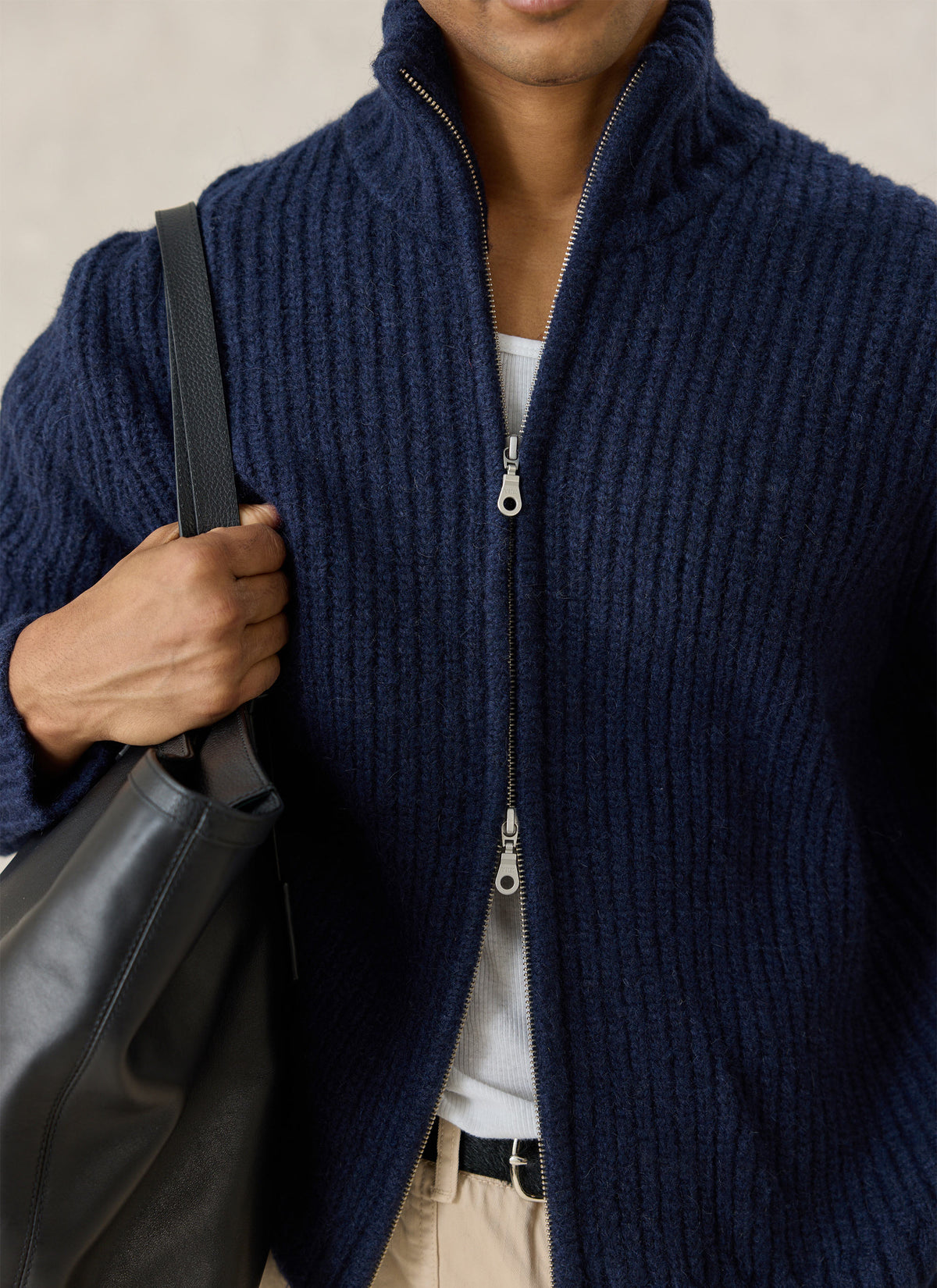 Close-up of the Percival navy Norton ribbed fisherman zip cardigan showing the high collar, two-way zipper, and a black bag.