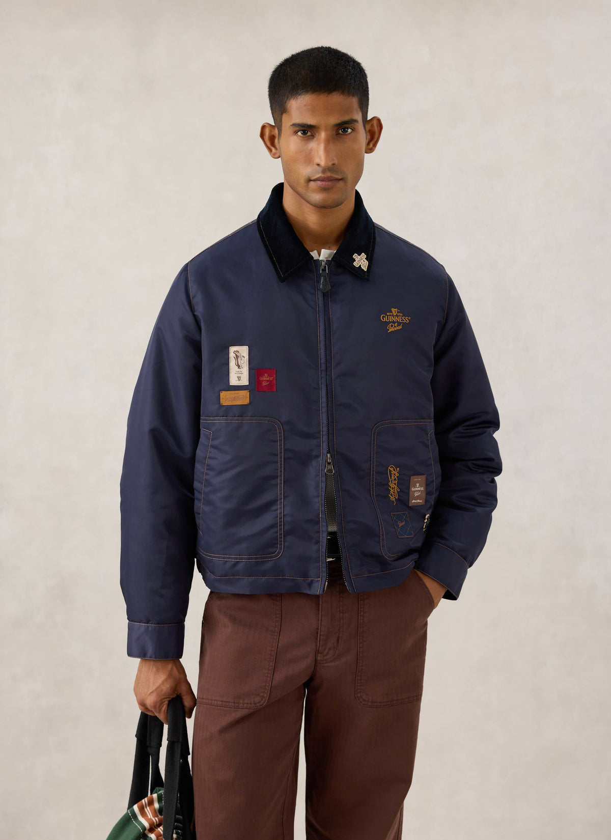 Model wearing the Guinness x Percival navy nylon jacket with contrast cord collar, embroidery, and patch details.
