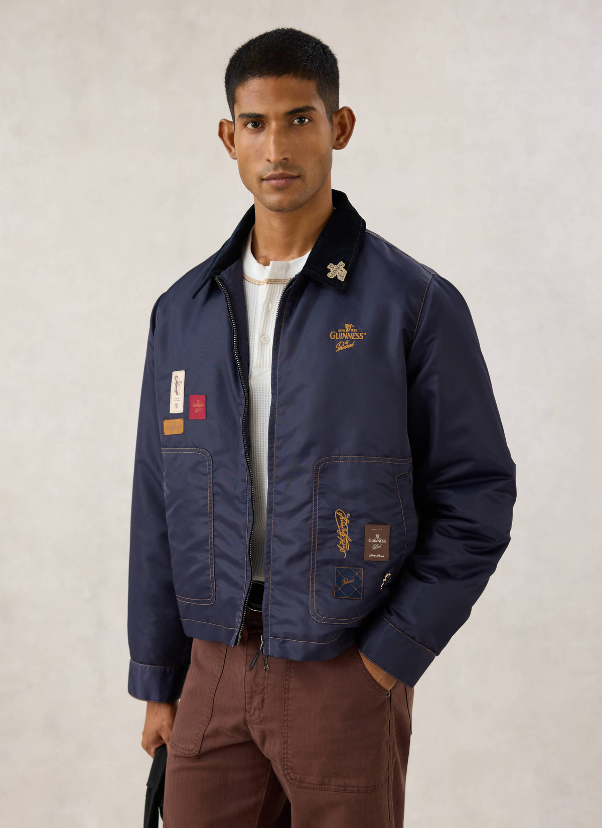 Model wearing the navy nylon Guinness x Percival jacket with cord collar and patches.