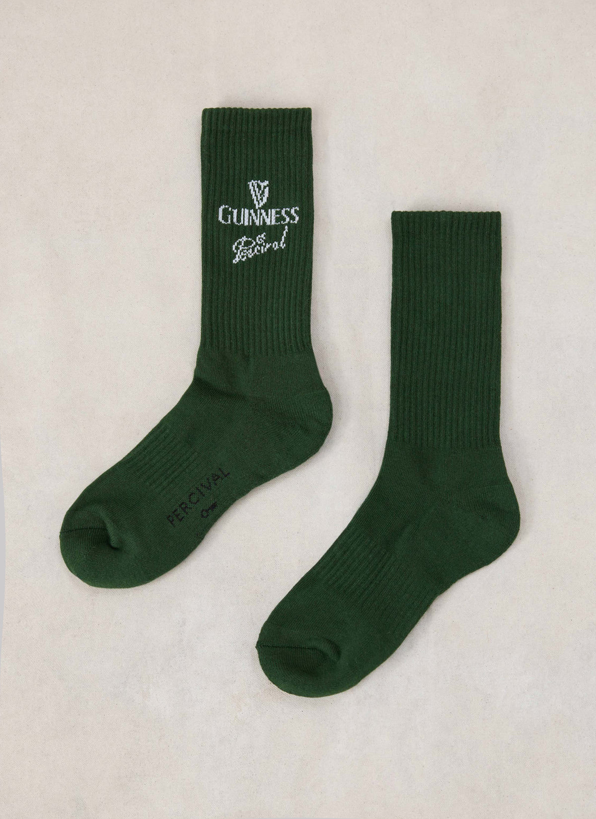 A pair of Guinness x Percival crew socks in forest green cotton blend with ribbed texture and knitted branding.