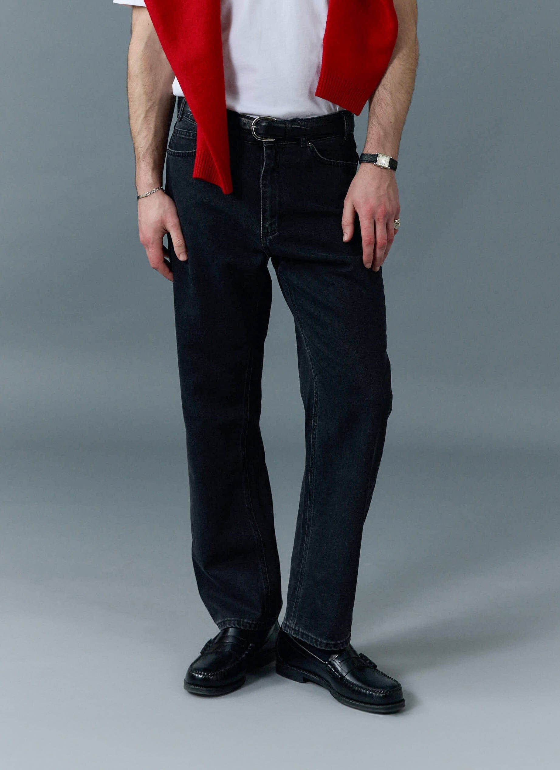 Model wears Percival black straight leg denim jeans with a white t-shirt, red sweater and black loafers.