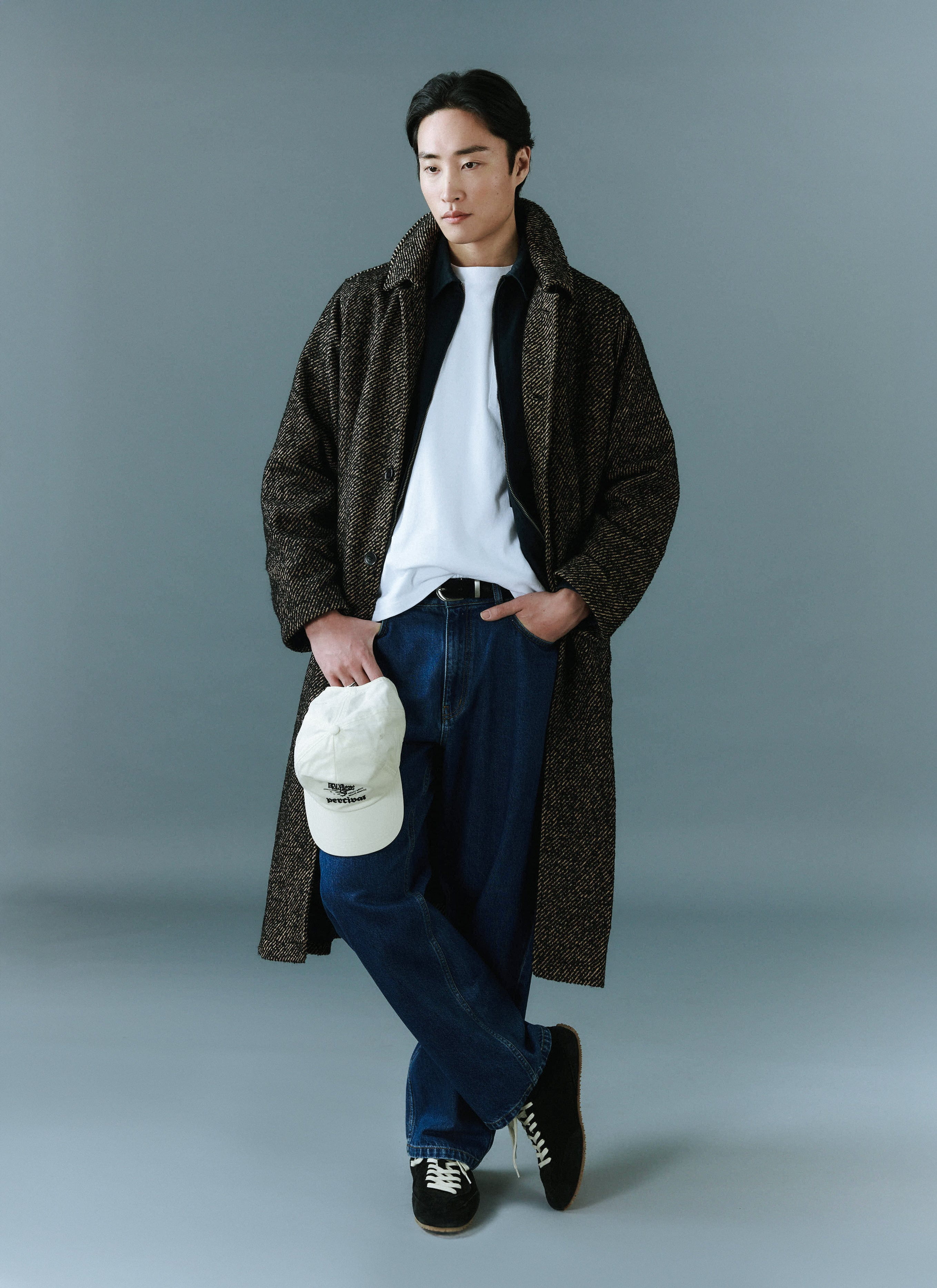 a model wears the percival menswear minnesota overcoat in oak herringbone twill with dark jeans and trainers.