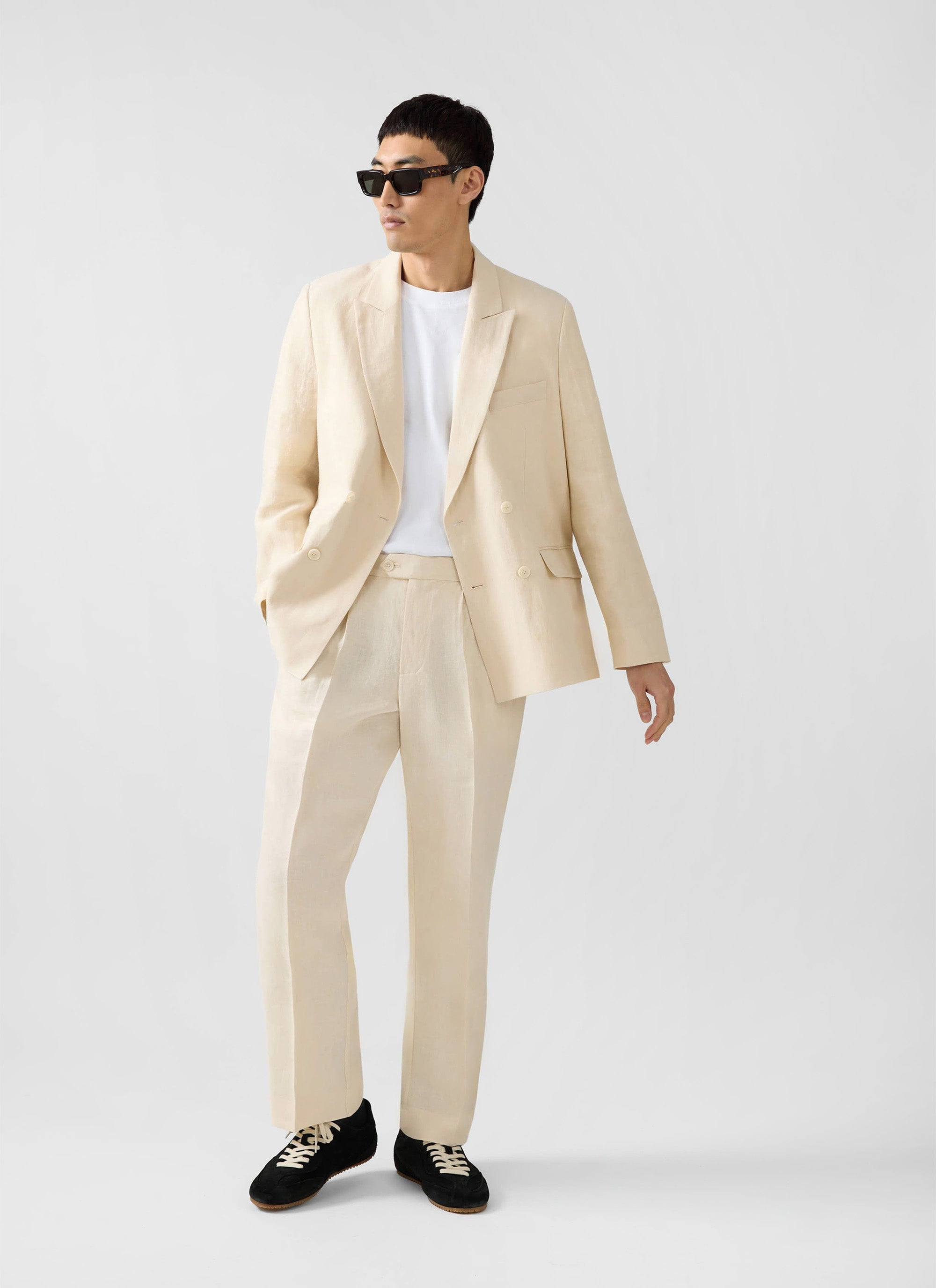 A model styles the Percival Clifton Double Breasted Blazer in cream linen with matching trousers and a white t-shirt.