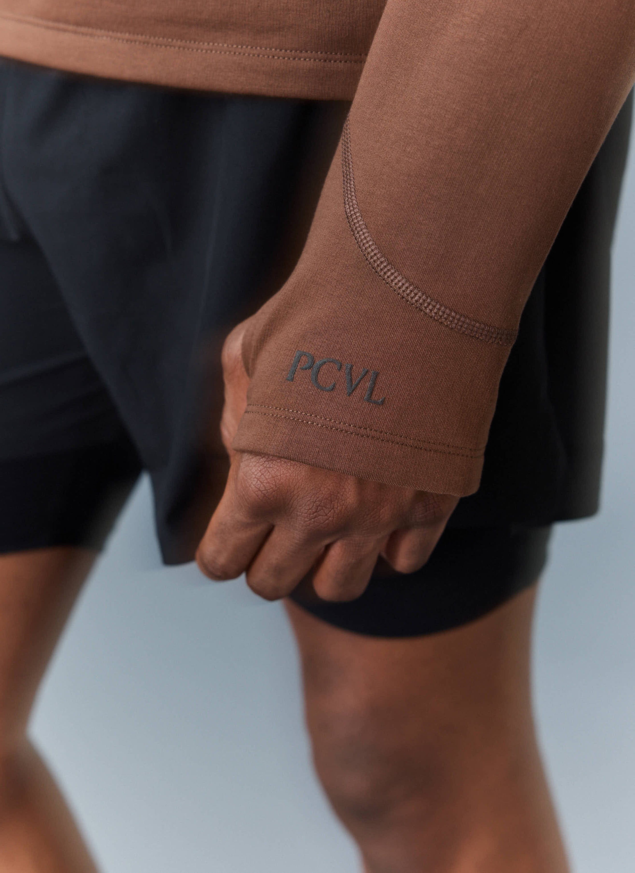 A close-up of the Percival PCVL Base Layer Quarter Zip in rust, showing the thumb loop and tonal PCVL logo on the cuff.