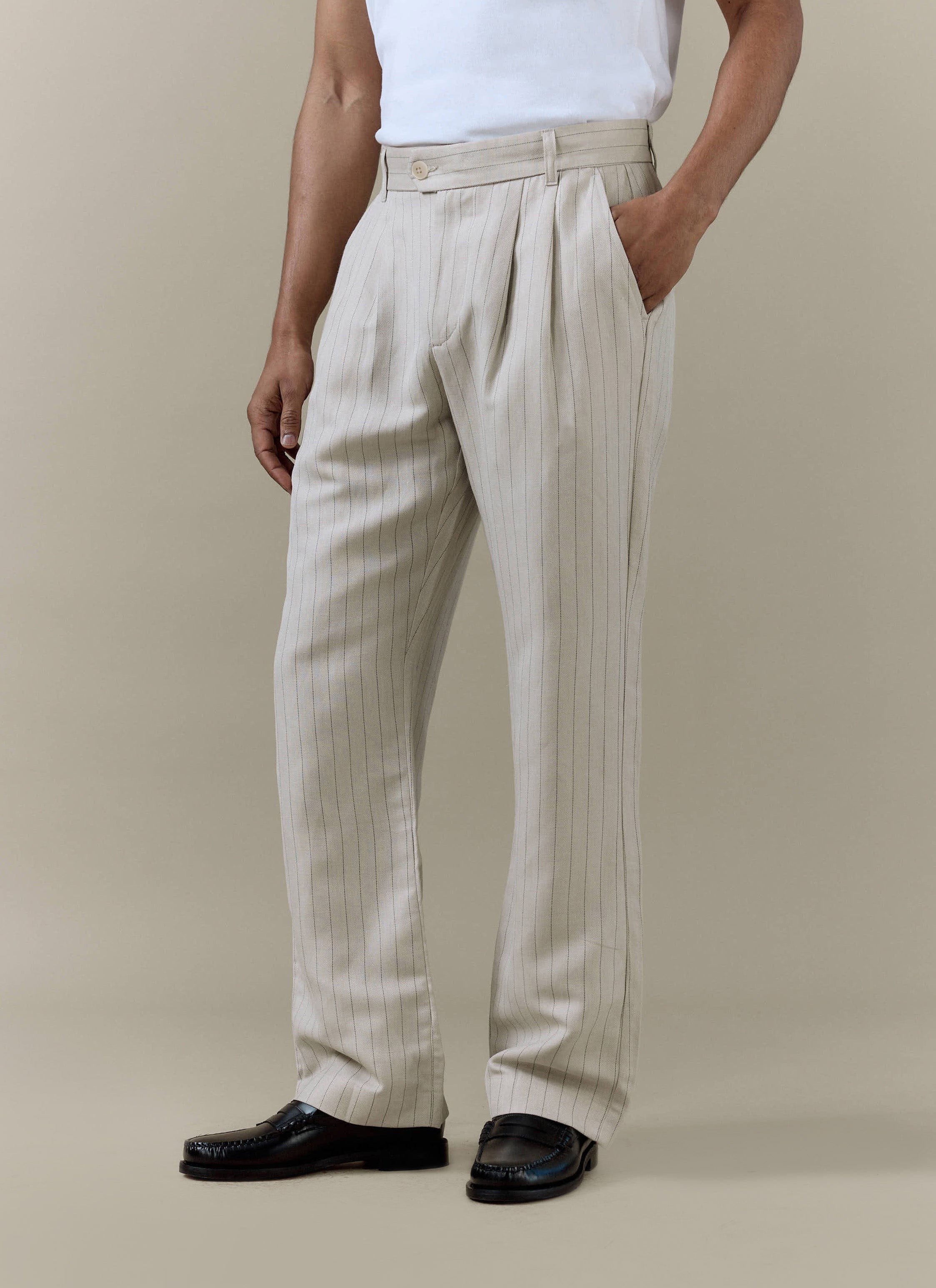 A model wears the cream striped pleated tailored trousers from Percival, styled with a white t-shirt and black loafers.