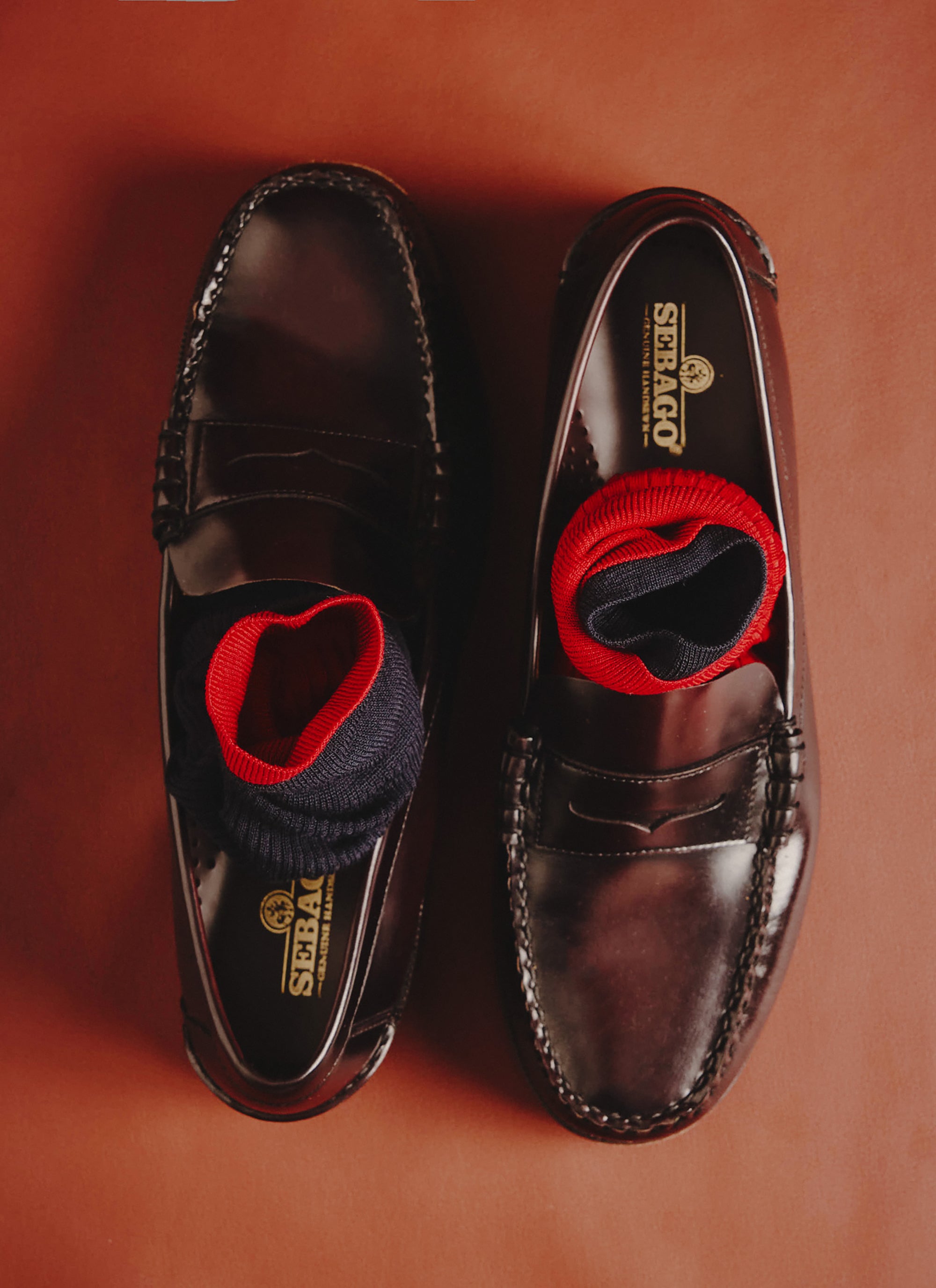 The red and navy Loafer Dress Socks from Percival, rolled and styled inside a pair of classic brown leather penny loafers.