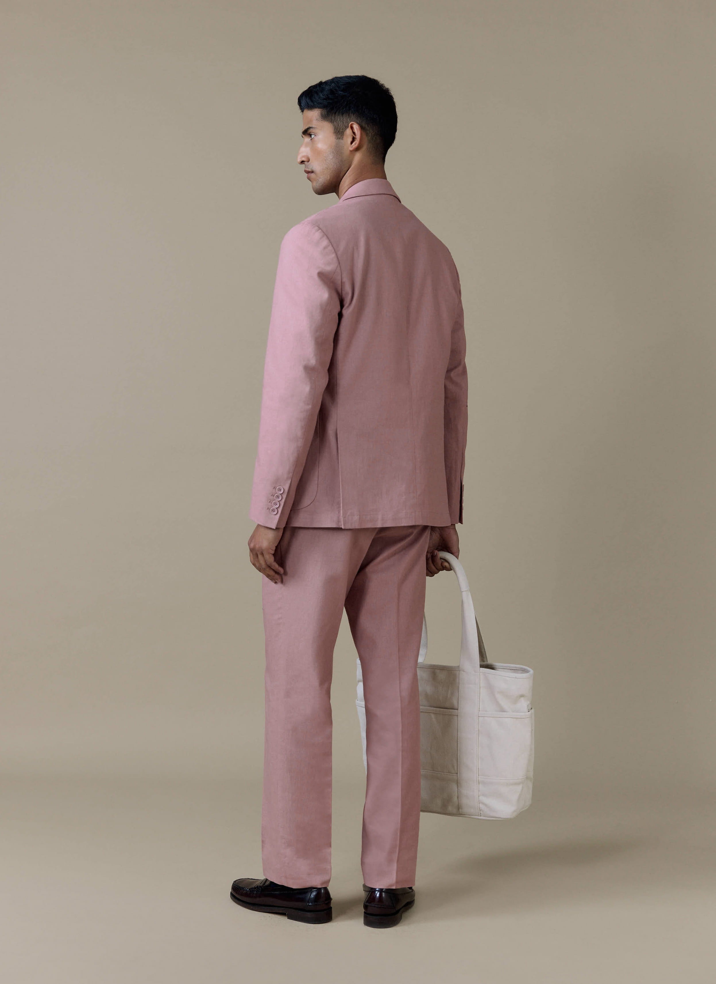 Rear view of the Percival tailored linen blazer and matching suit trousers in dusty pink, styled with a cream tote bag.