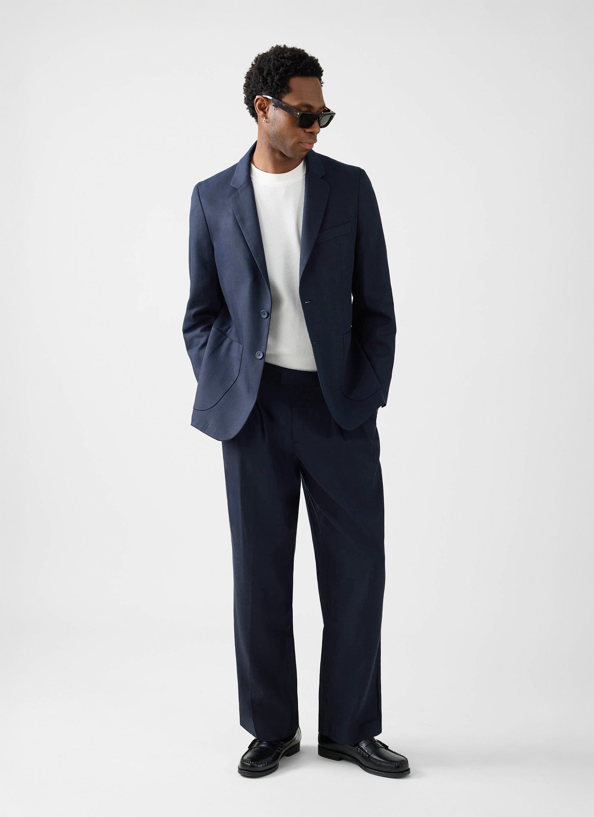 A model wears the Percival Lyocell Regular Blazer and Trousers in navy, styled with a white t-shirt and sunglasses.