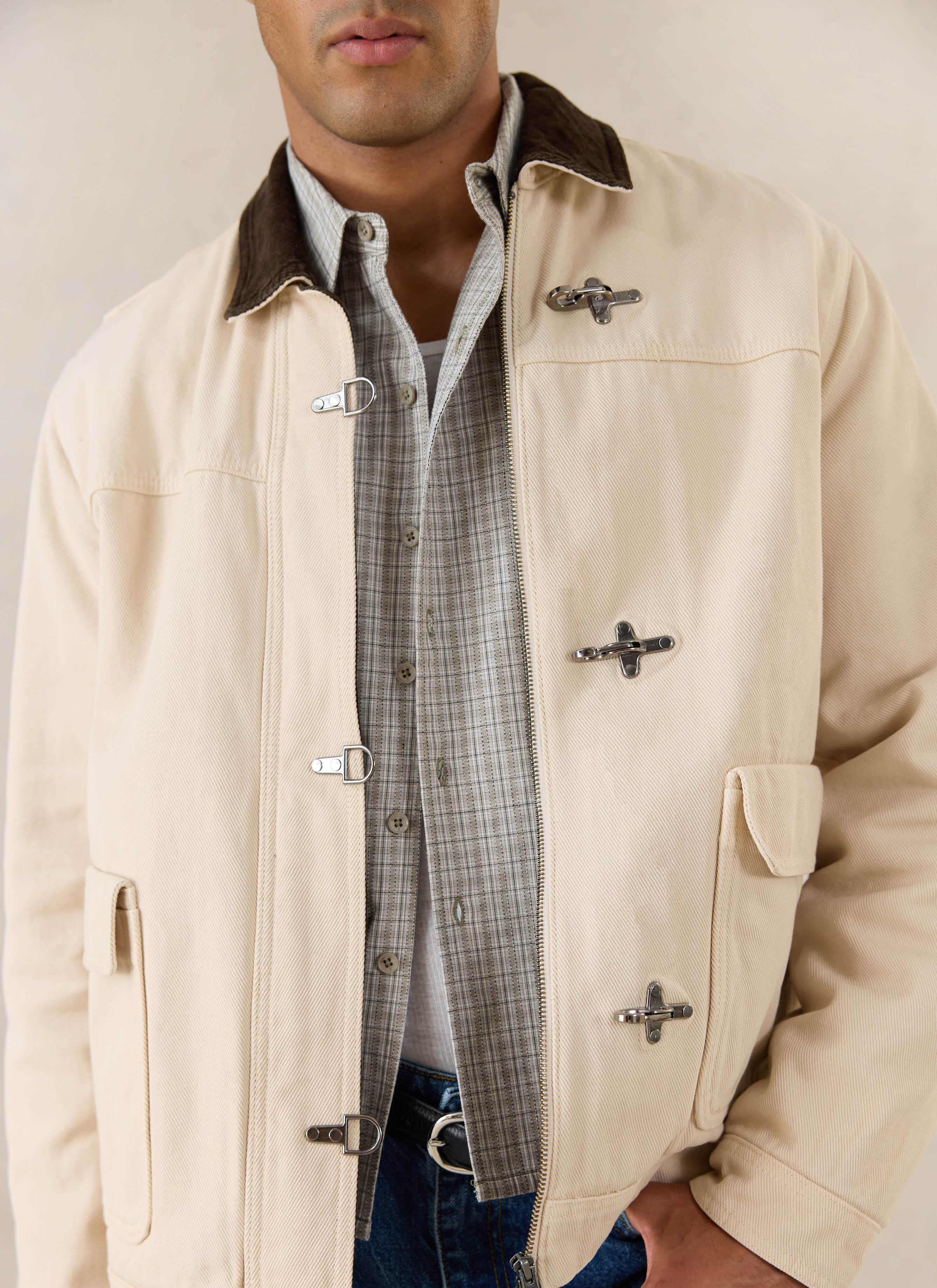 A close-up of a model wearing the cream Percival Fontane jacket with its brown corduroy collar and metal clasp details.