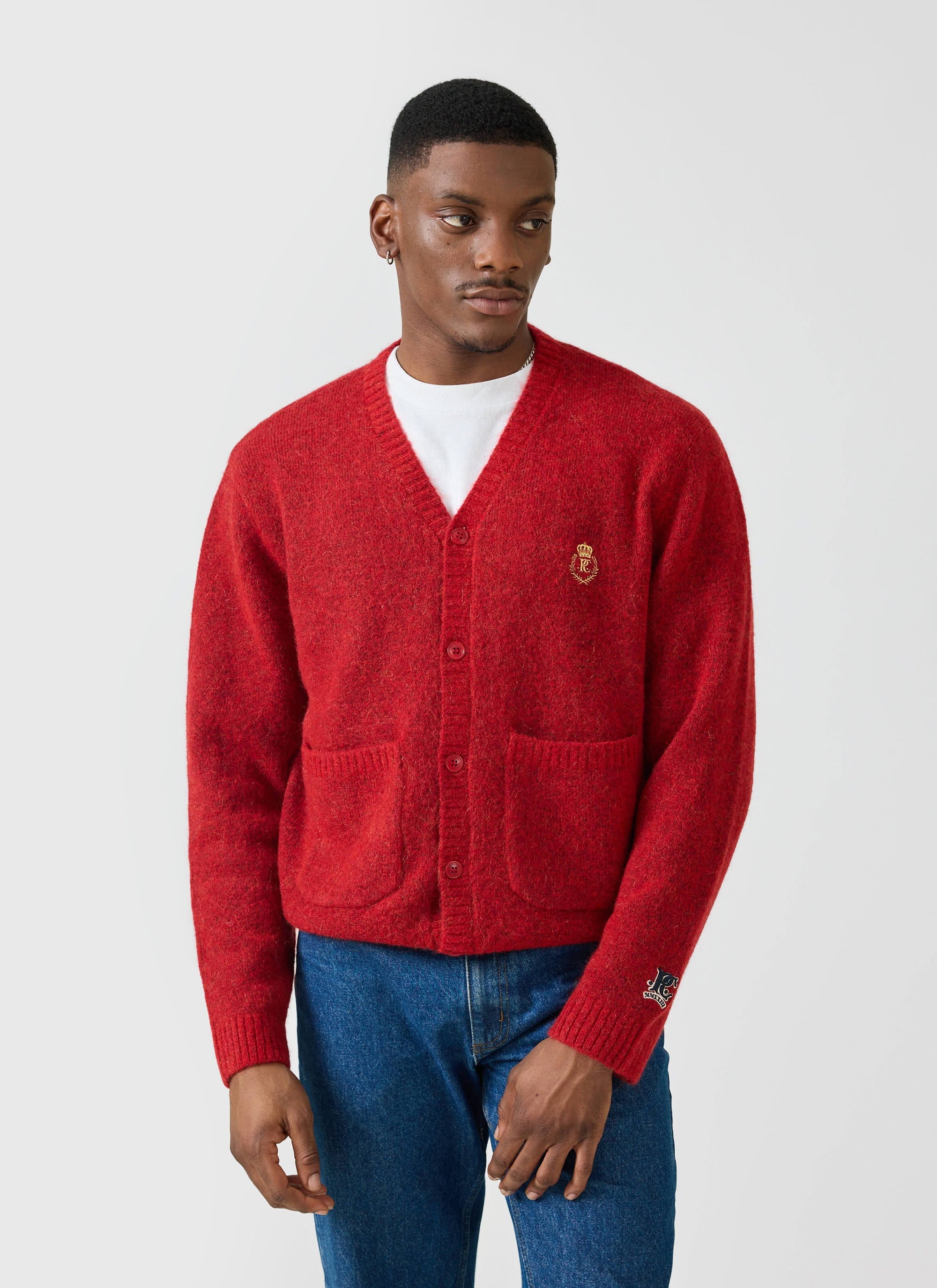 A man models the red Champion x Percival White Glove knitted cardigan, styled with a white t-shirt and blue jeans.