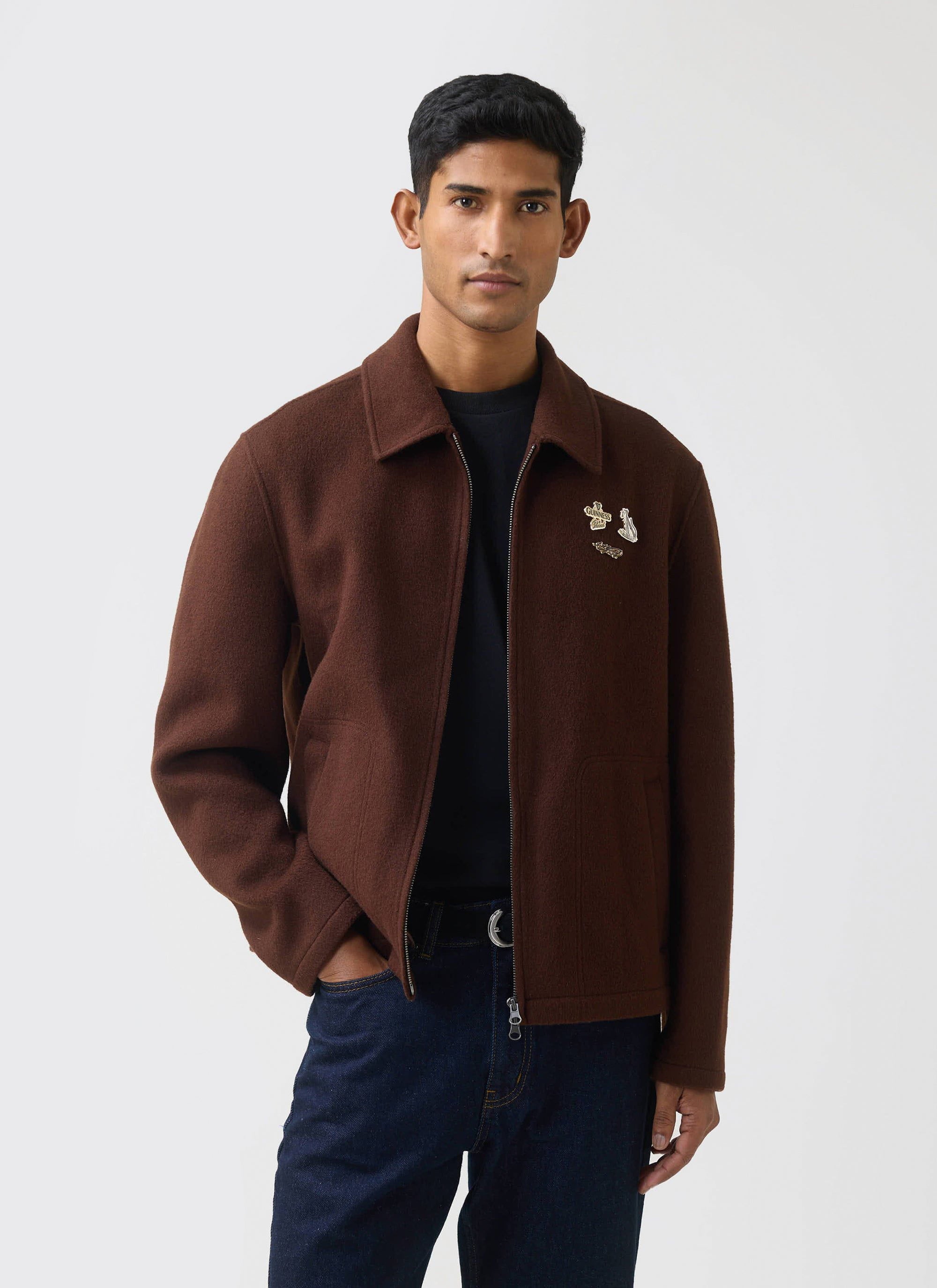 A man models the Guinness x Percival wool jacket in espresso brown, styled over a black tee and dark wash jeans.