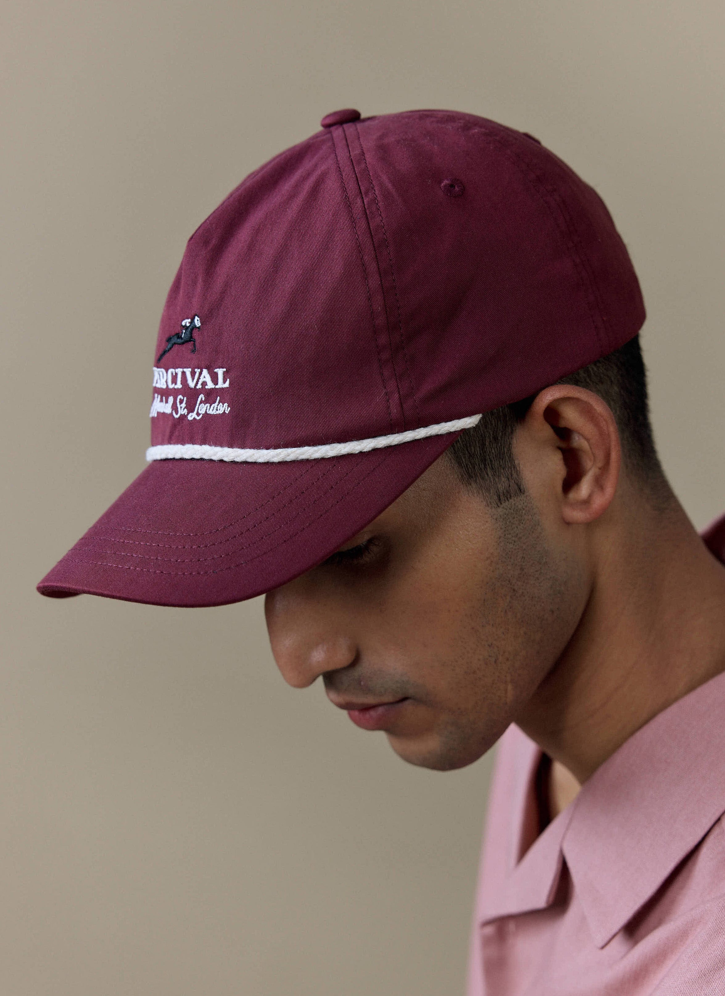 Close-up of a model wearing the red Percival Tournament Soft Trucker Cap with white rope detail and embroidery.