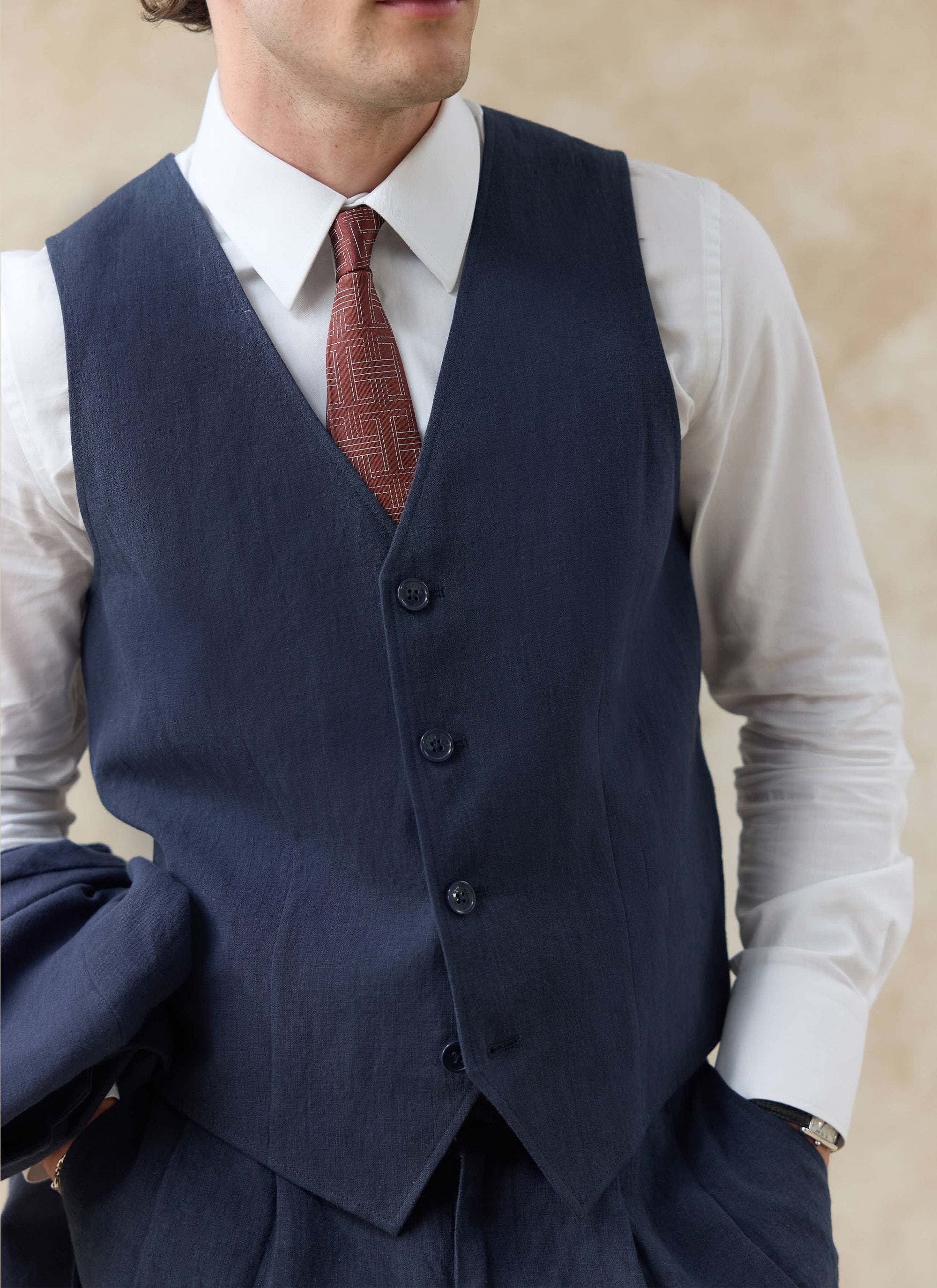 Percival navy blue linen waistcoat with a three-button front, layered over a white shirt and patterned tie.