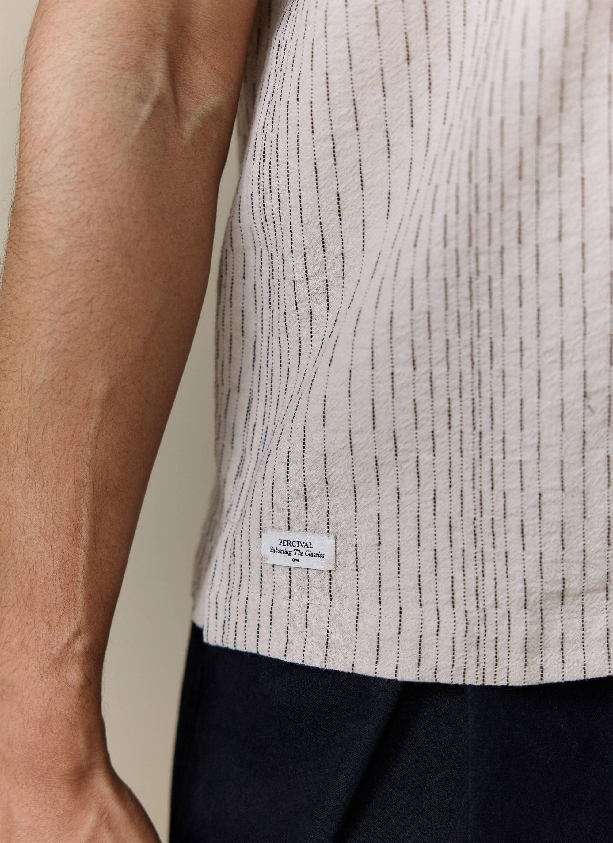 Close-up of the textured ecru cotton with vertical stitching and branded label on the Percival Leland Cuban Shirt.