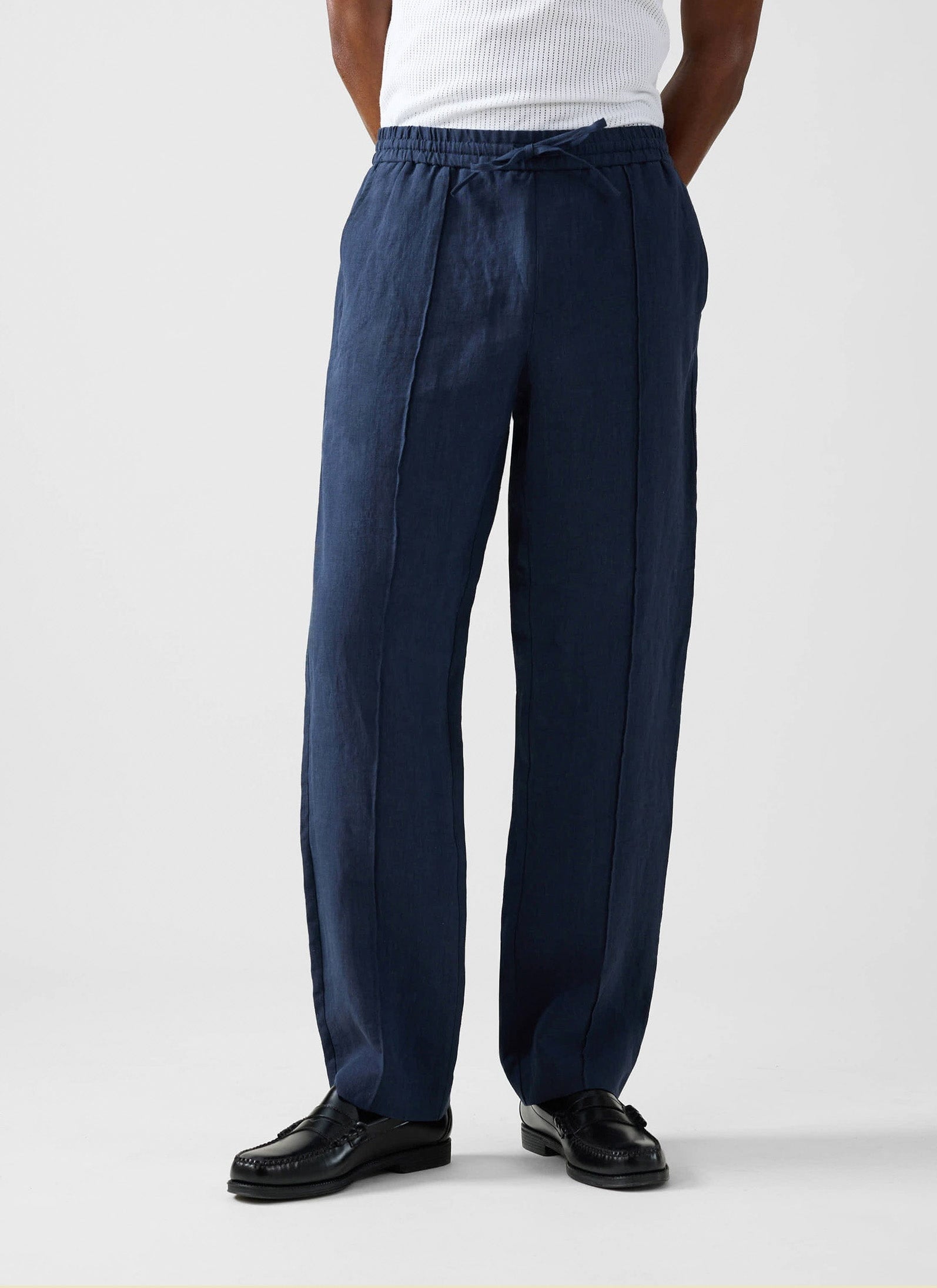 A model wears the Percival Lorena Wide Leg Trousers in navy linen, styled with a white vest and black leather loafers.