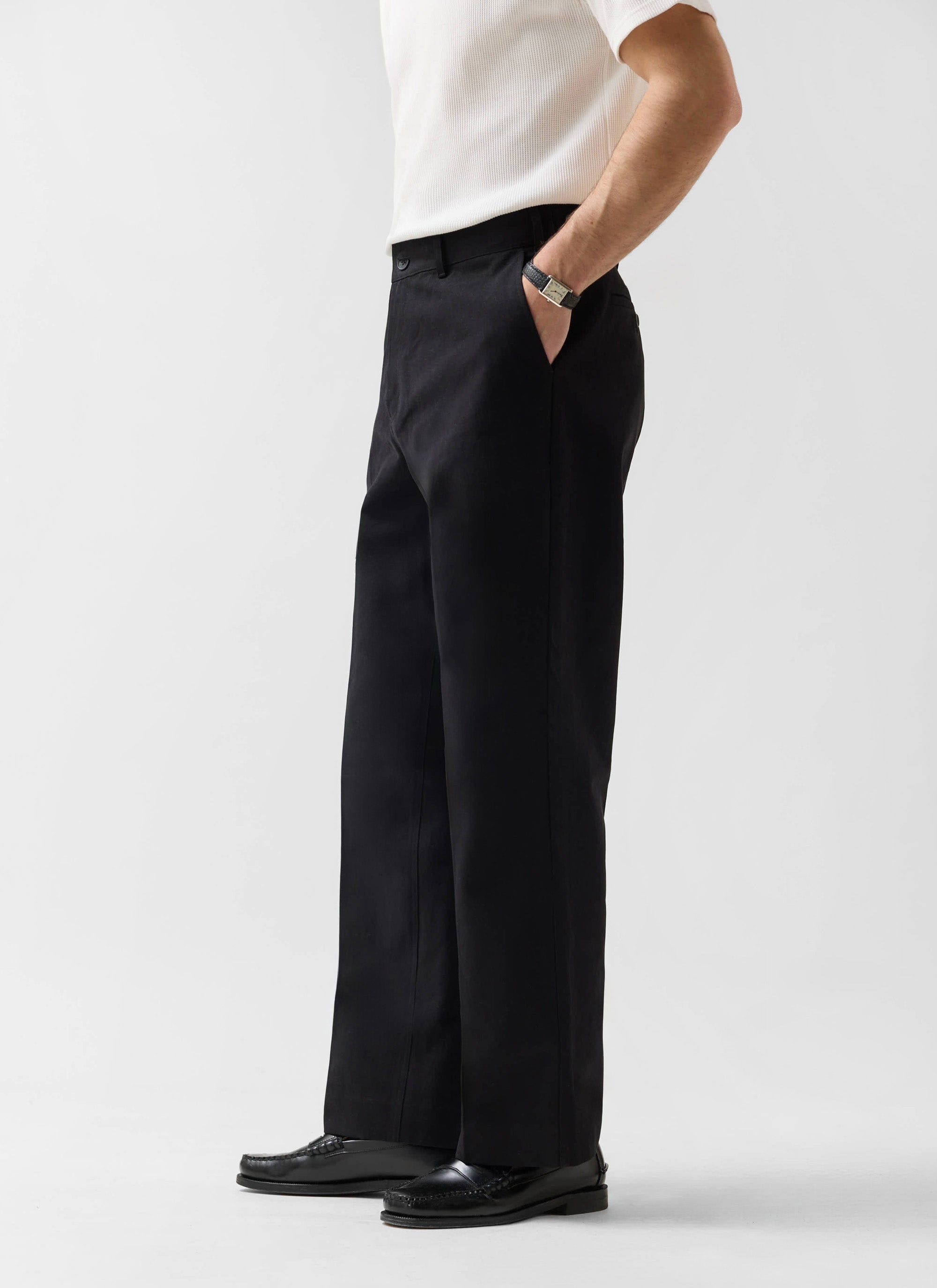 Side view of a model wearing the Percival Wide Leg Chino in black, paired with a white ribbed top and black loafers.