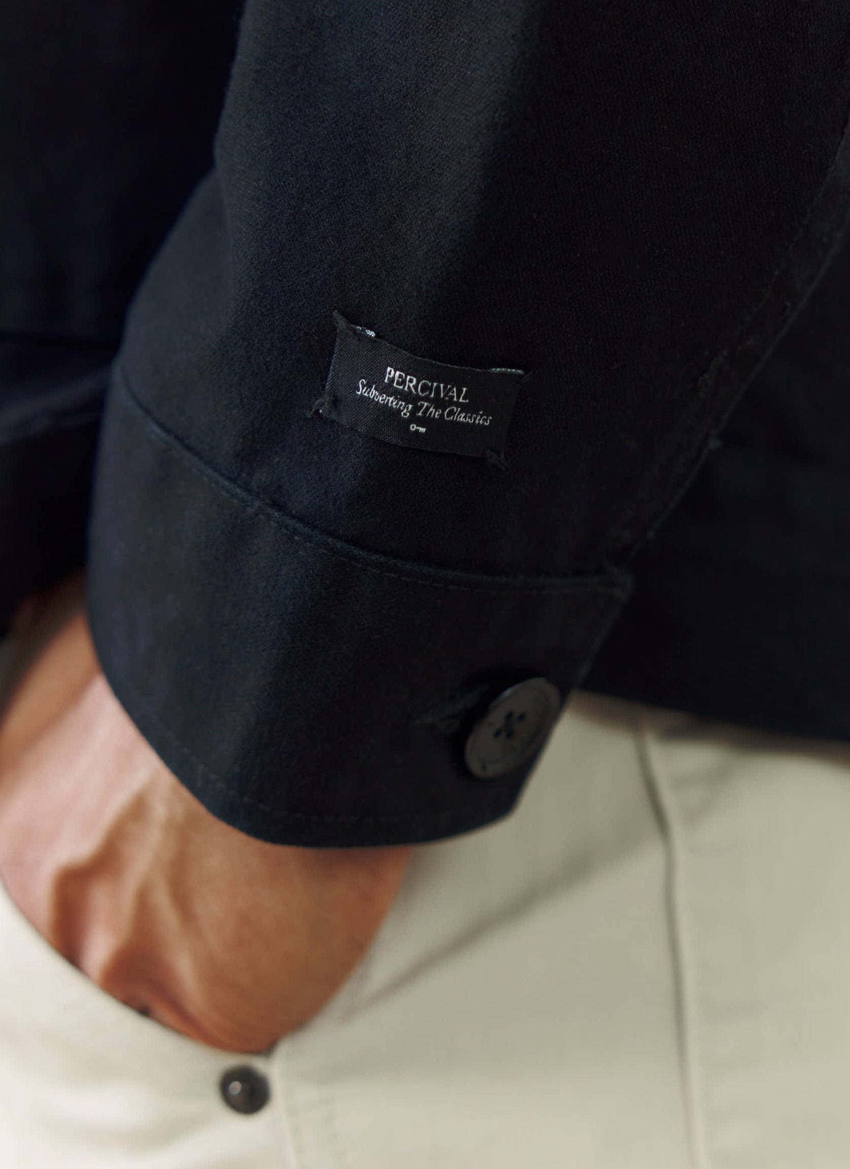 A close-up of the Percival branded label on the sleeve of the black cotton Ernst Jacket.