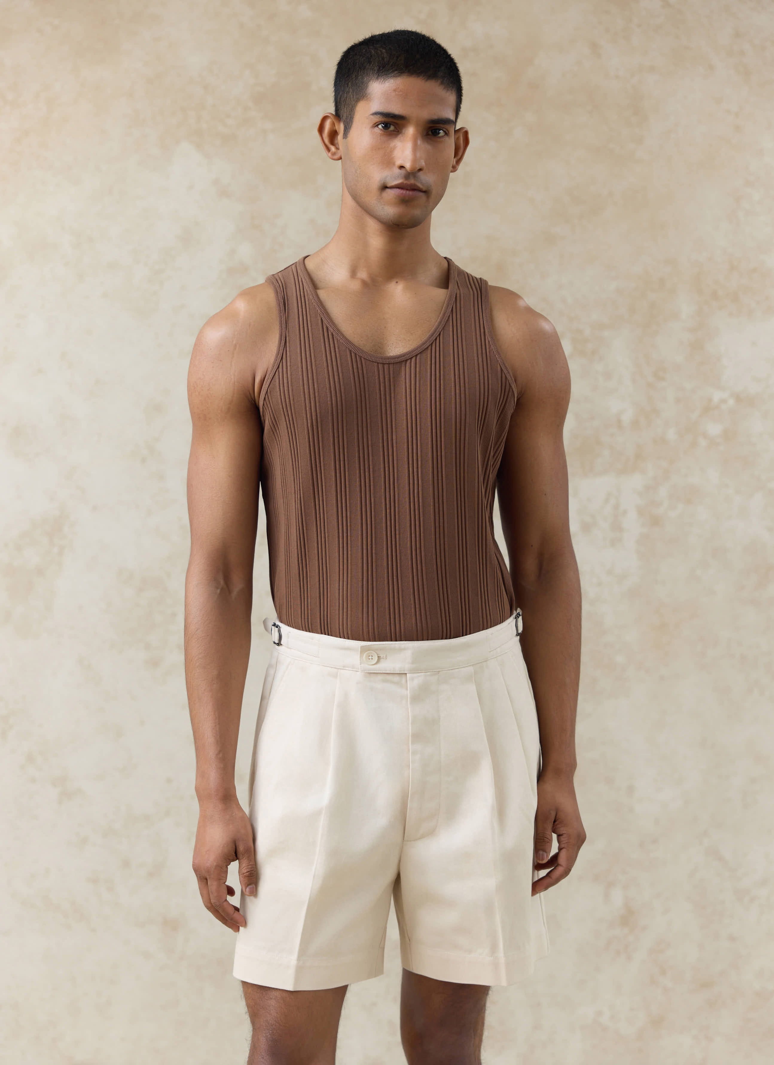 Brown ribbed cotton Percival Leon vest and cream Blake double pleated cotton shorts worn by a model.