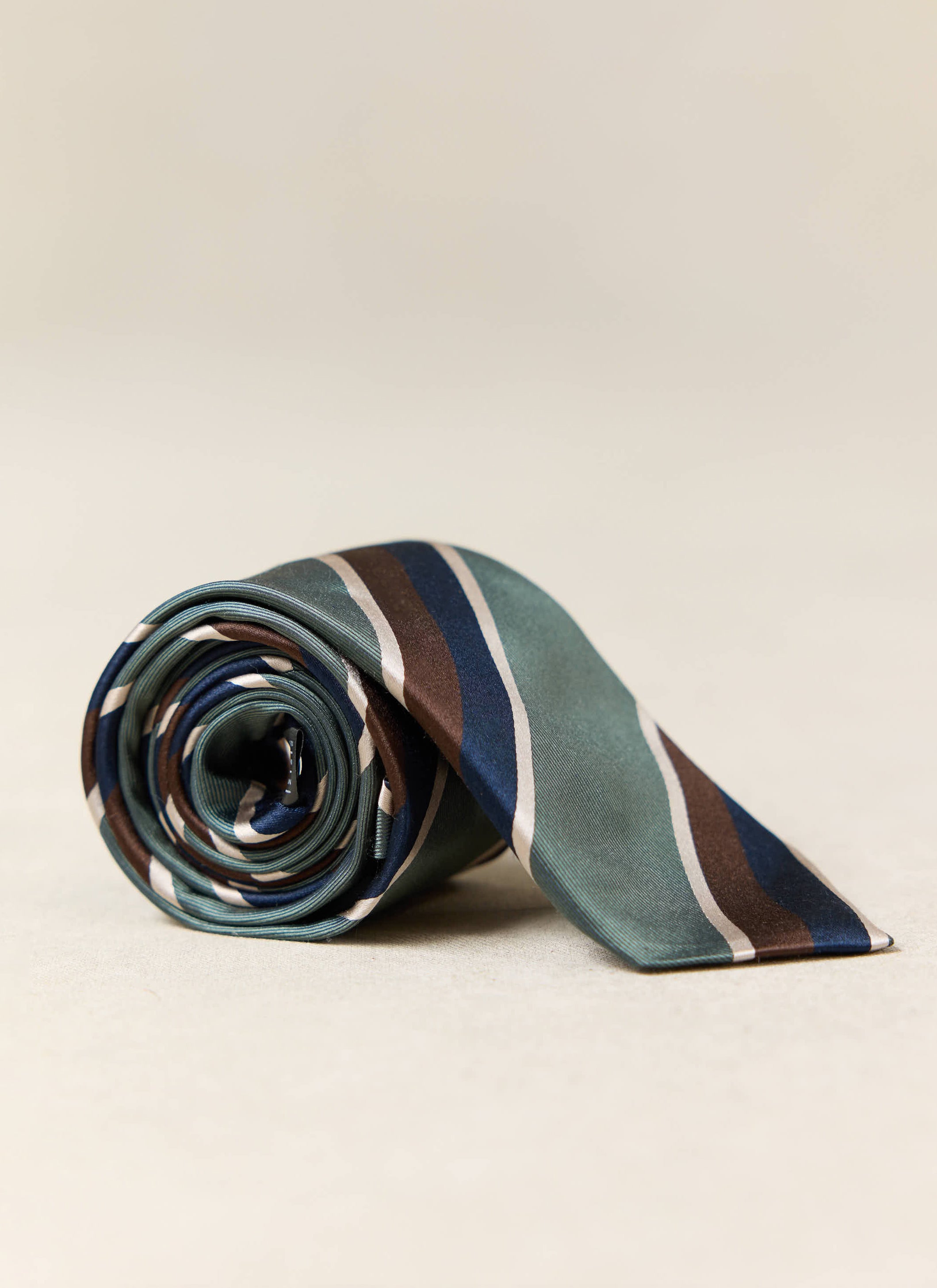 Multi, a rolled-up forest green silk tie featuring navy, brown and cream stripes.