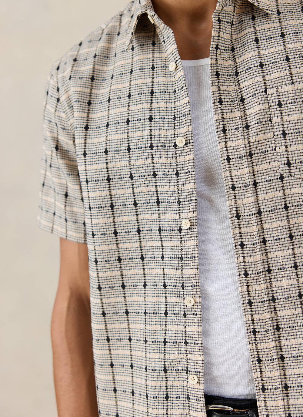 A close-up of a model wearing the cream Percival textured check shirt, styled over a white ribbed vest.