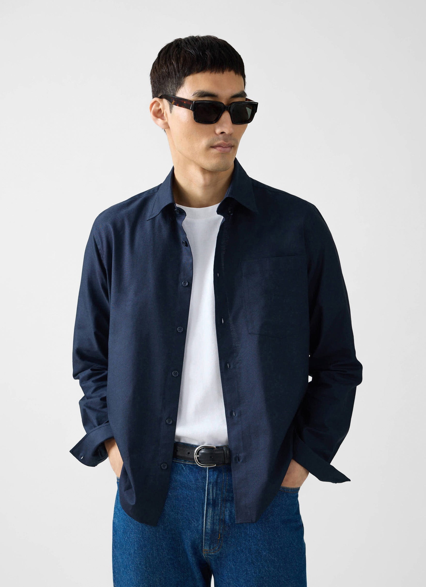 A model wears the Percival navy Oxford Regular Shirt open over a white t-shirt and jeans, with sunglasses on.
