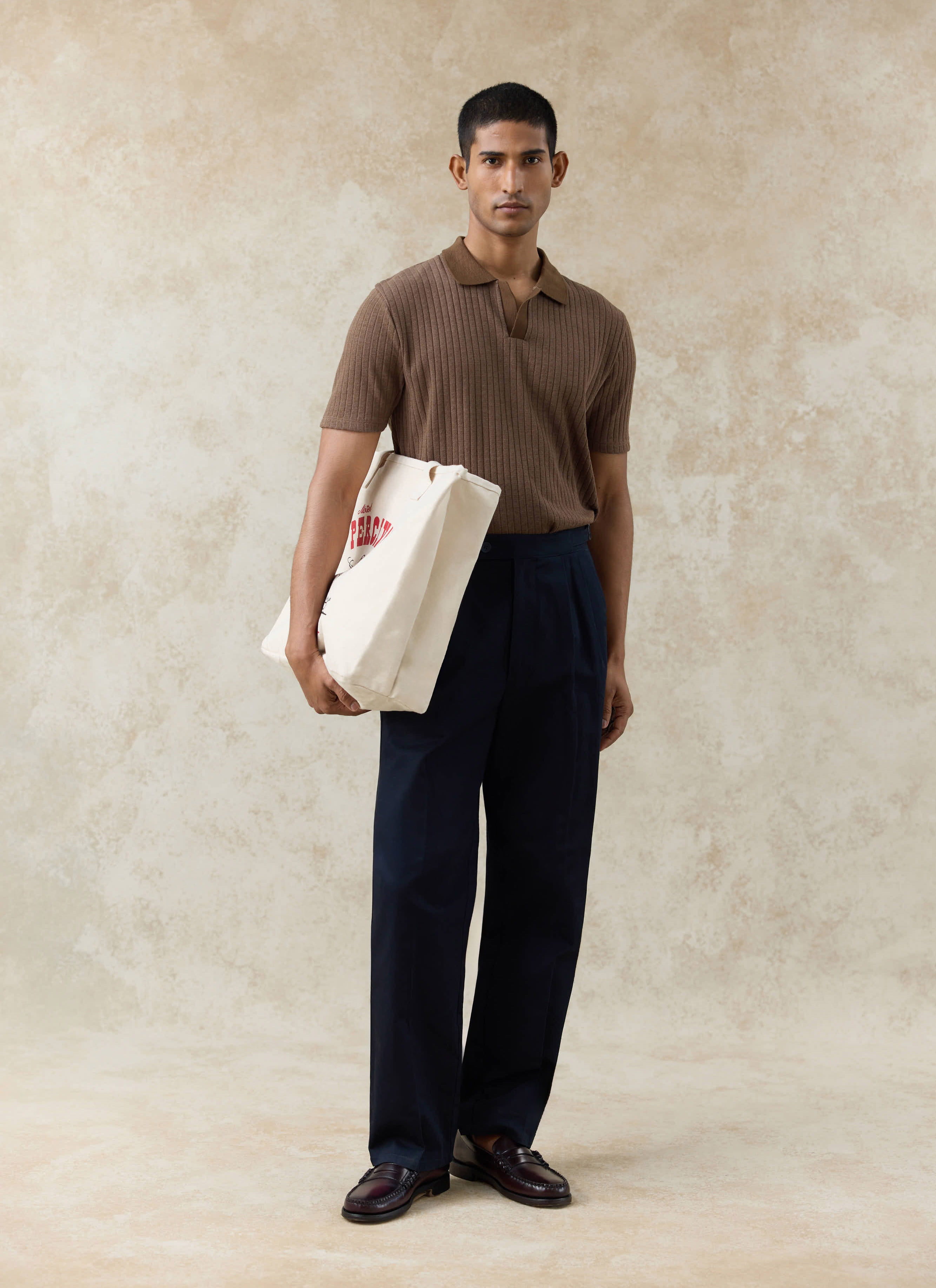 Espresso Percival Anthony Ribbed Polo and navy cotton Blake Double Pleated Trousers with a cream branded tote bag.