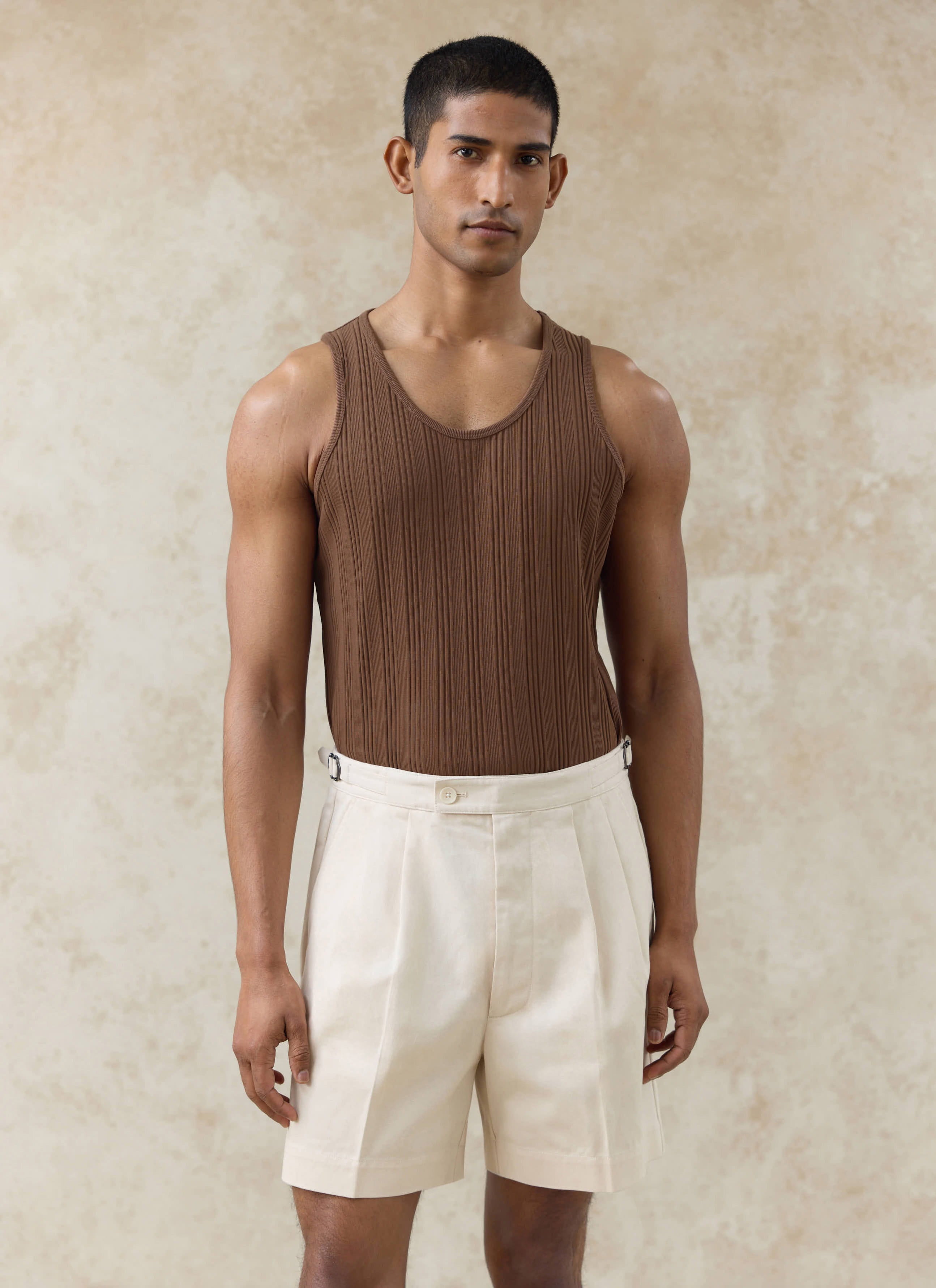 Model wearing the brown Leon Ribbed Vest in organic cotton by Percival, styled with off-white tailored shorts.