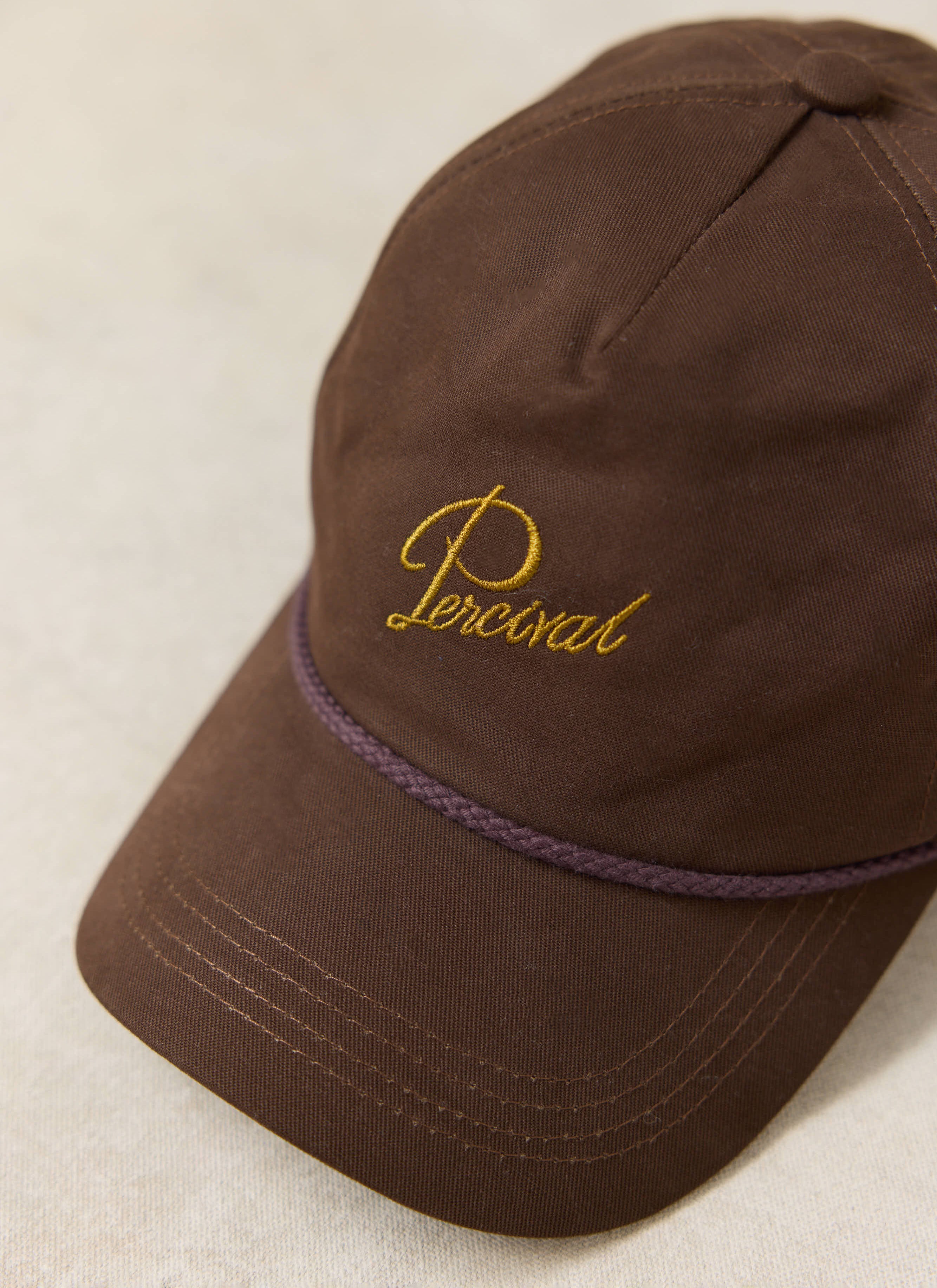 Close-up of the espresso brown Percival Luther Soft Trucker Cap in brushed cotton with gold script embroidery.