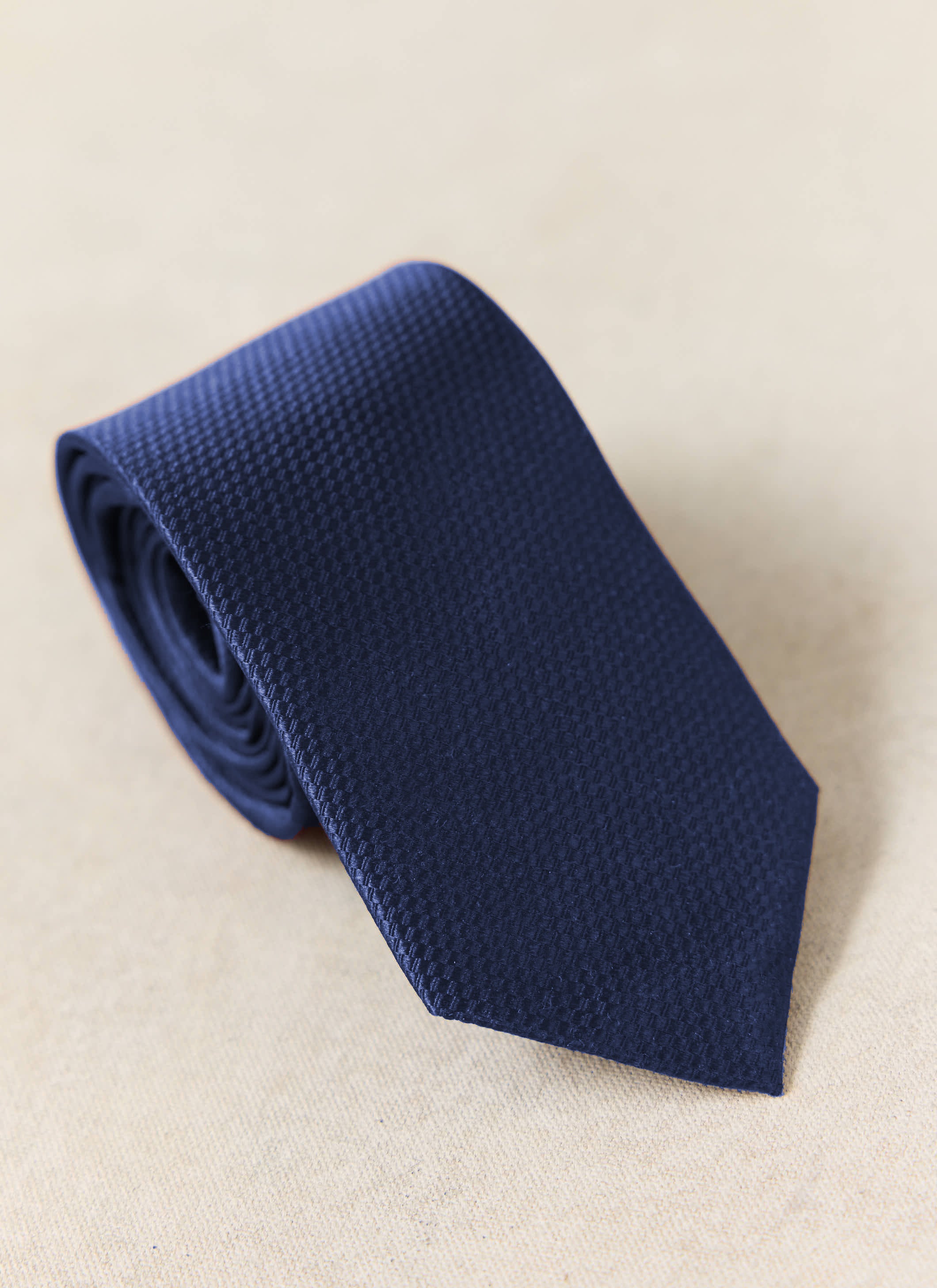 Percival Grenadine Tie in Navy Silk, featuring a textured weave and shown rolled up on a neutral background.