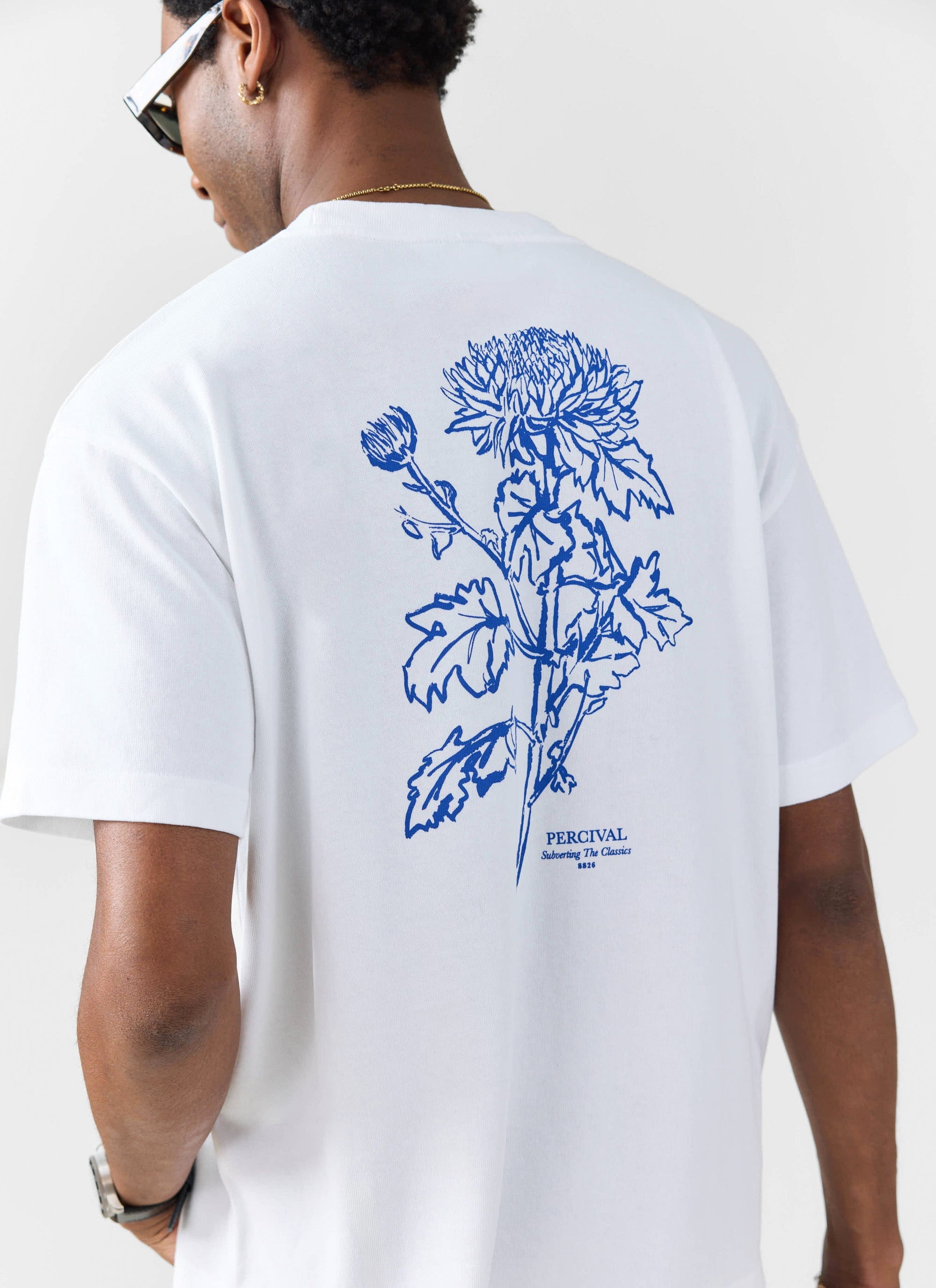 A man models the back of the white Smith Floral oversized t-shirt from Percival, showing the blue floral illustration.