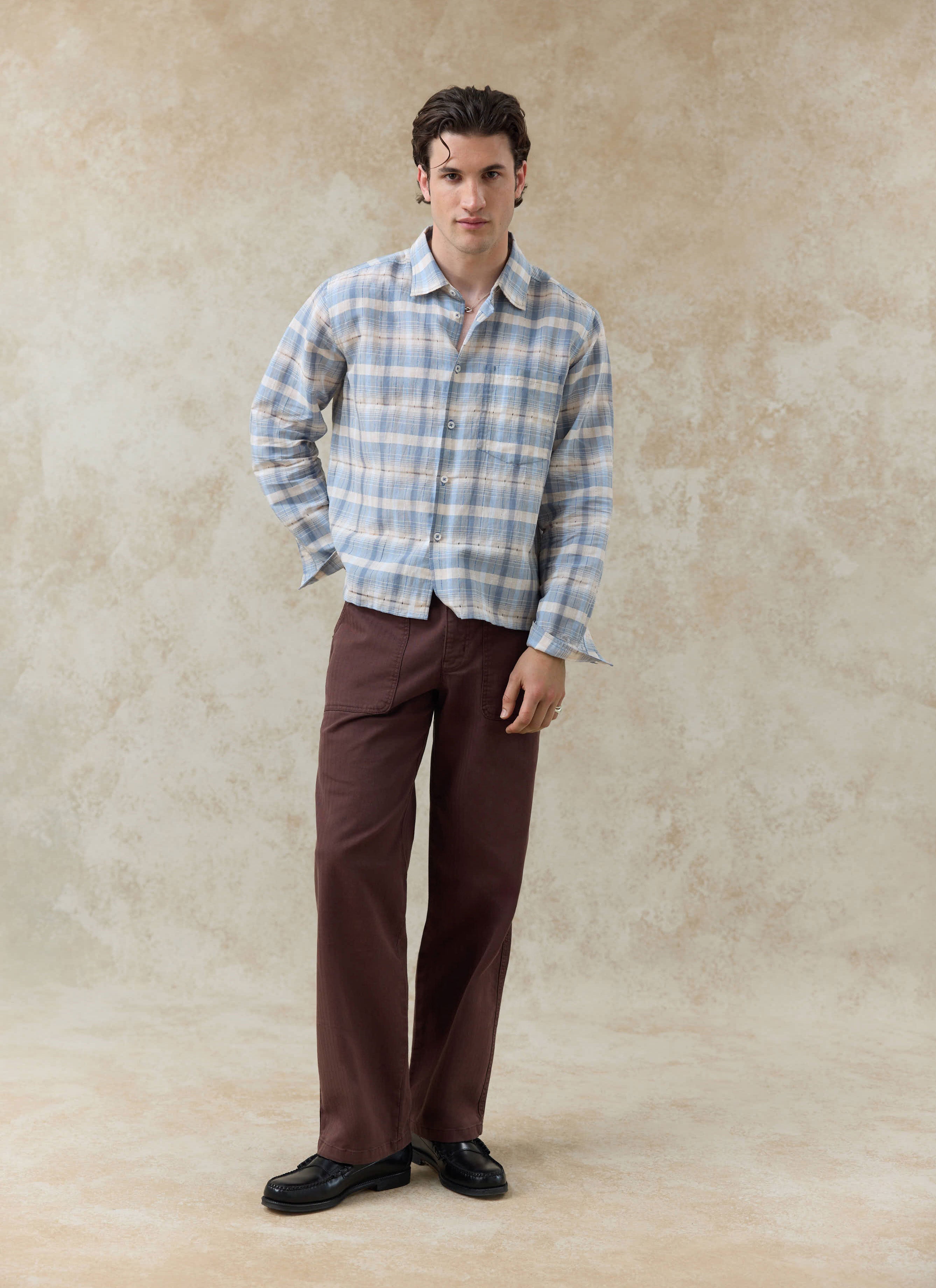 The Percival Jesse Cropped Shirt in a blue check linen-cotton blend, worn by a model with brown trousers.