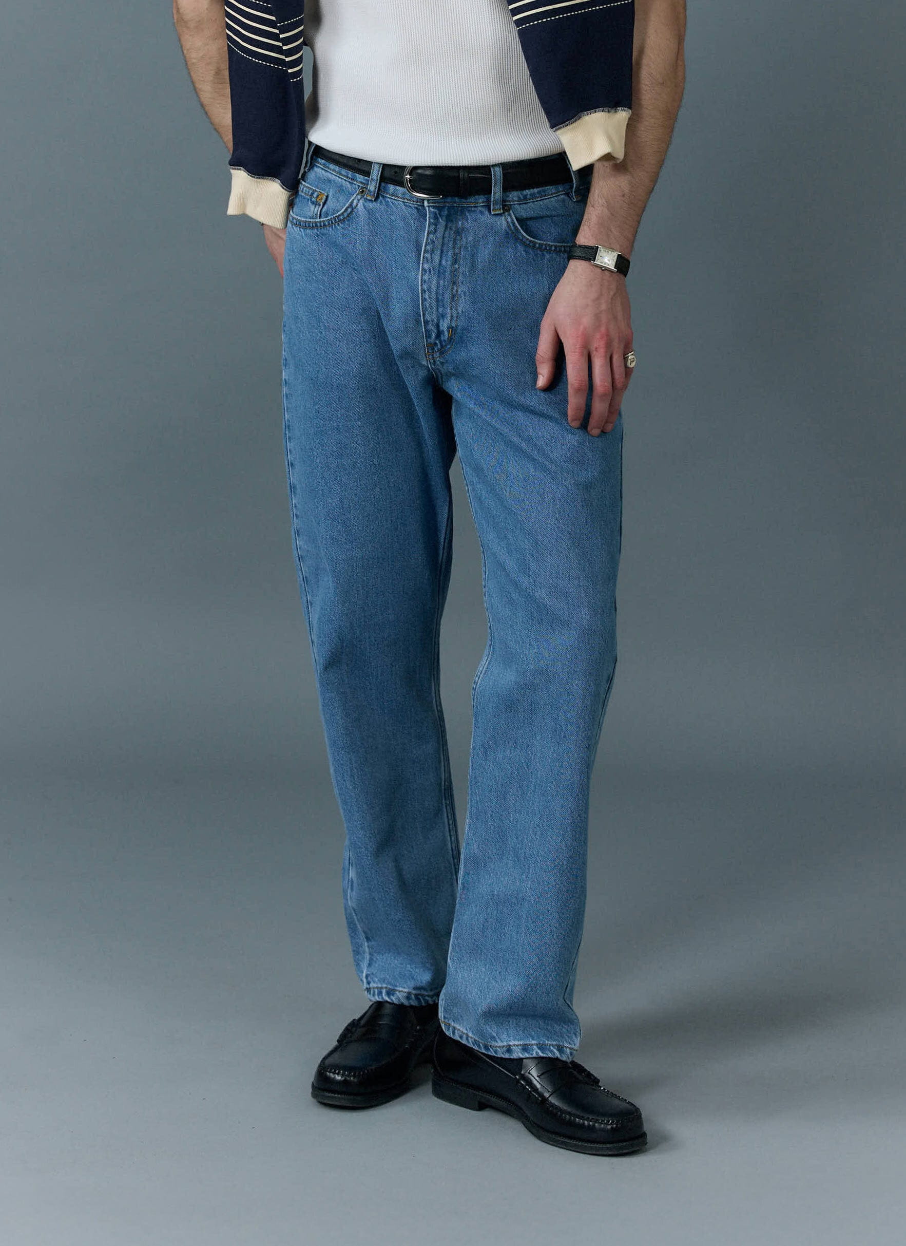 Model wearing Percival light wash blue straight leg denim jeans with a black belt and loafers.