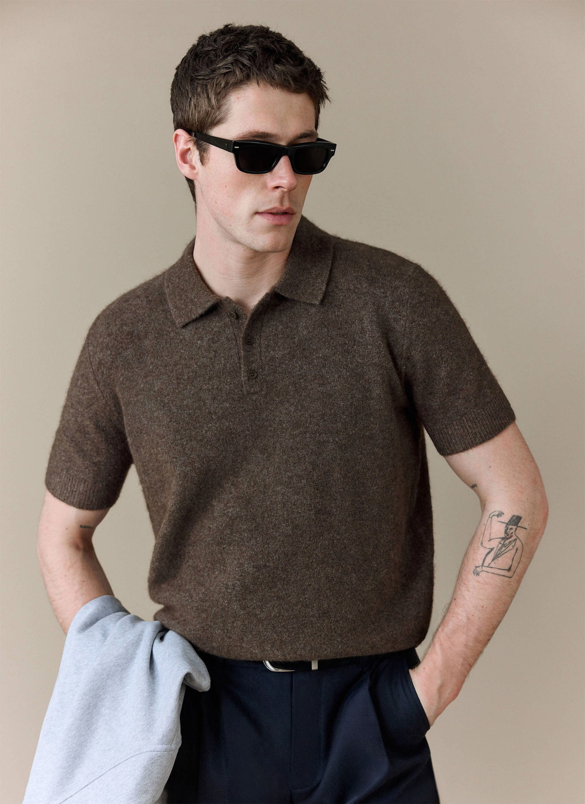 A model wears the Percival Collins Boxy Knitted Polo in Espresso, styled with sunglasses and dark trousers.
