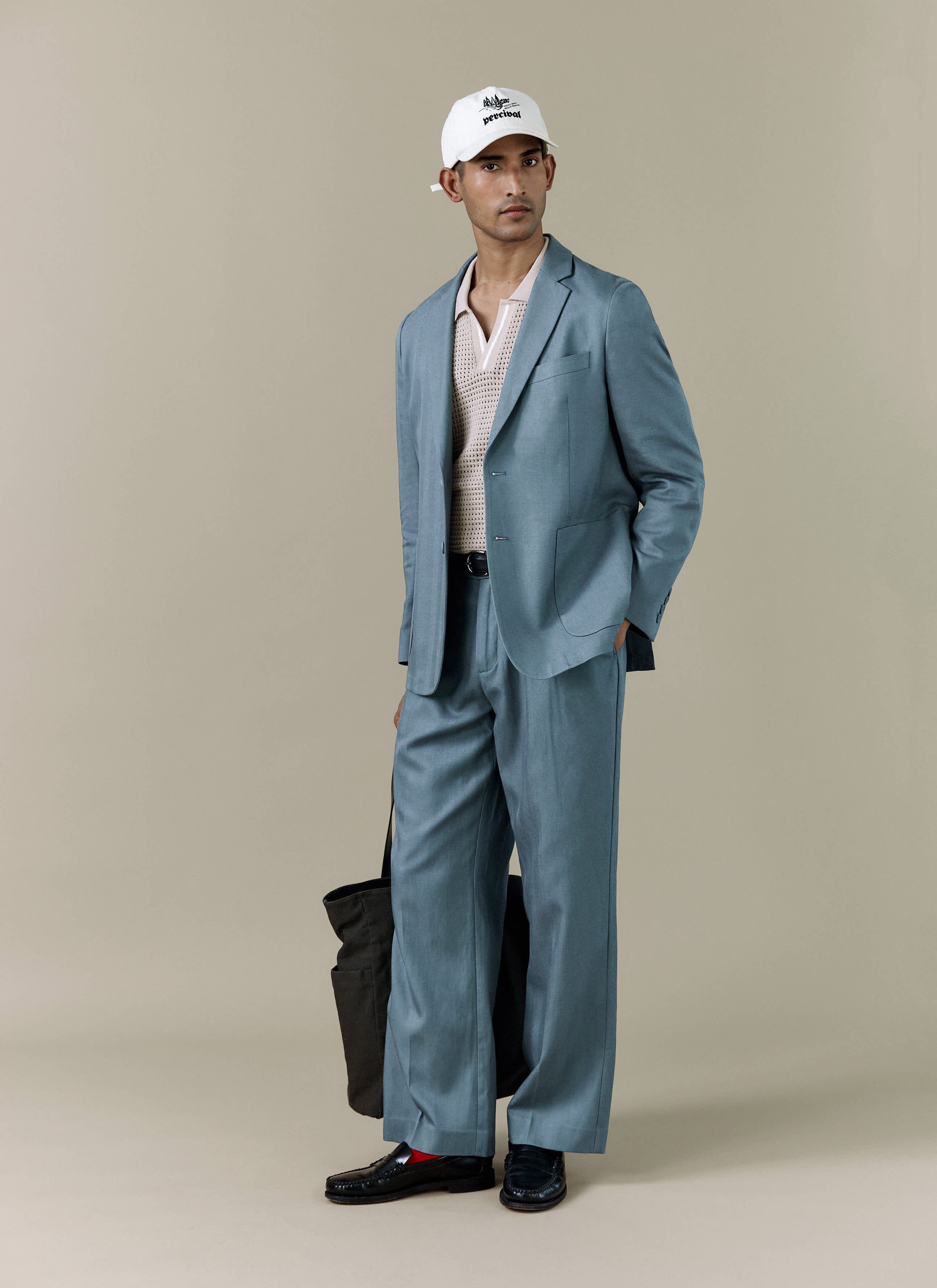 A model wears the Percival Lyocell Regular Blazer in Slate Blue with matching trousers, a white cap, and black loafers.