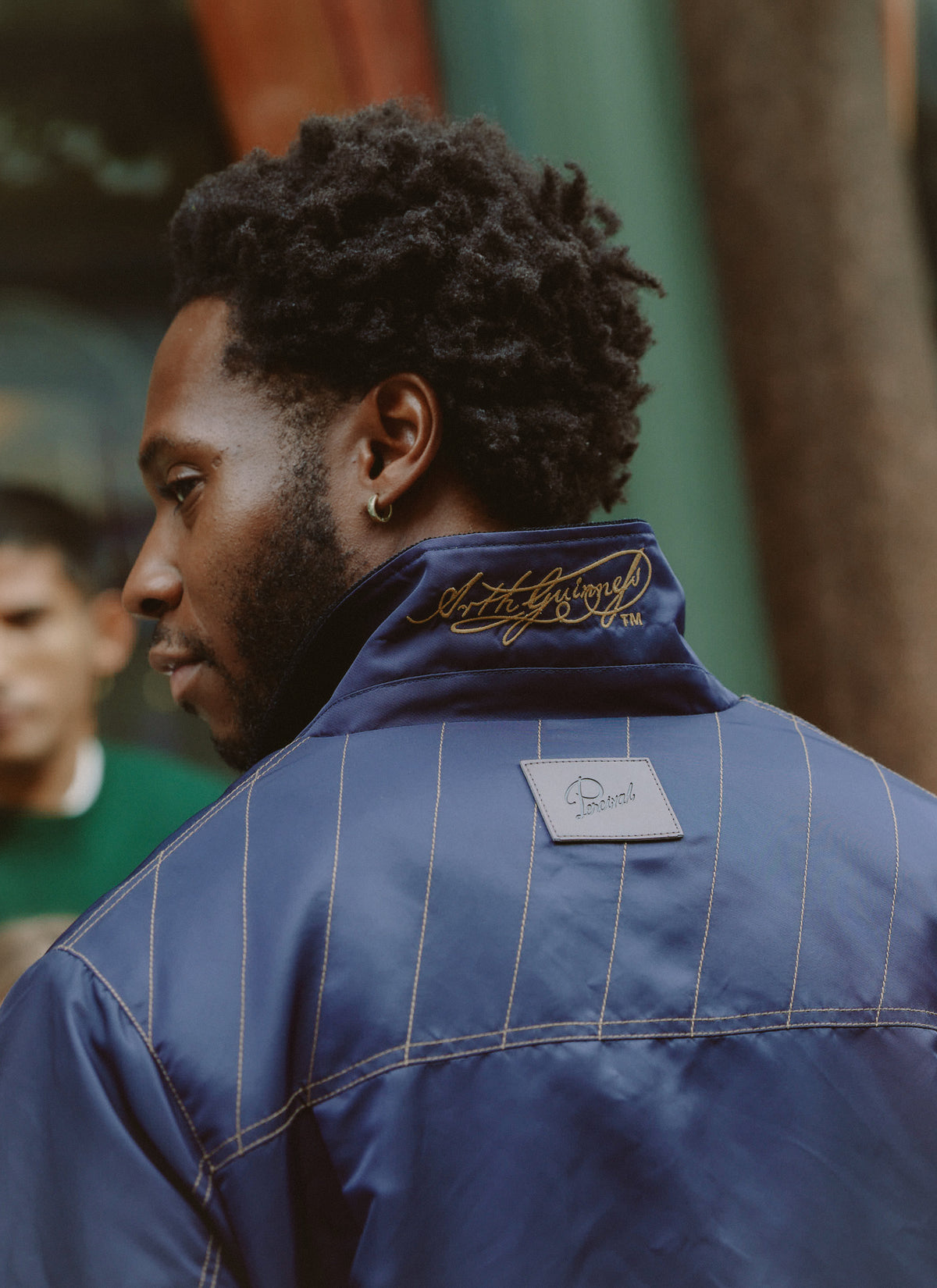 Close-up of a model wearing the Guinness x Percival navy nylon jacket, showing the embroidered collar and leather tab trim.