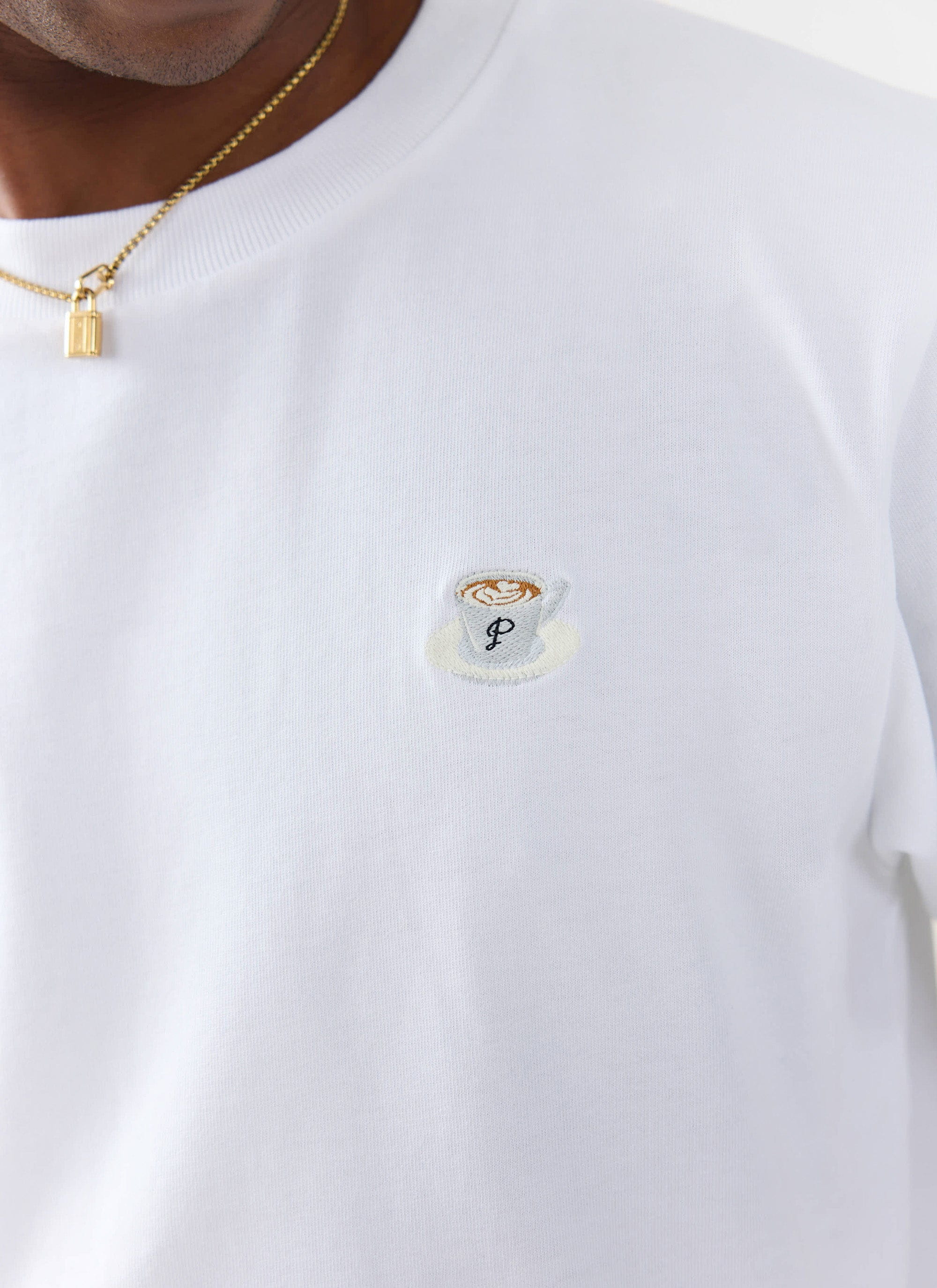 A close-up of the latte cup embroidery on the chest of the white organic cotton T-shirt from Percival.